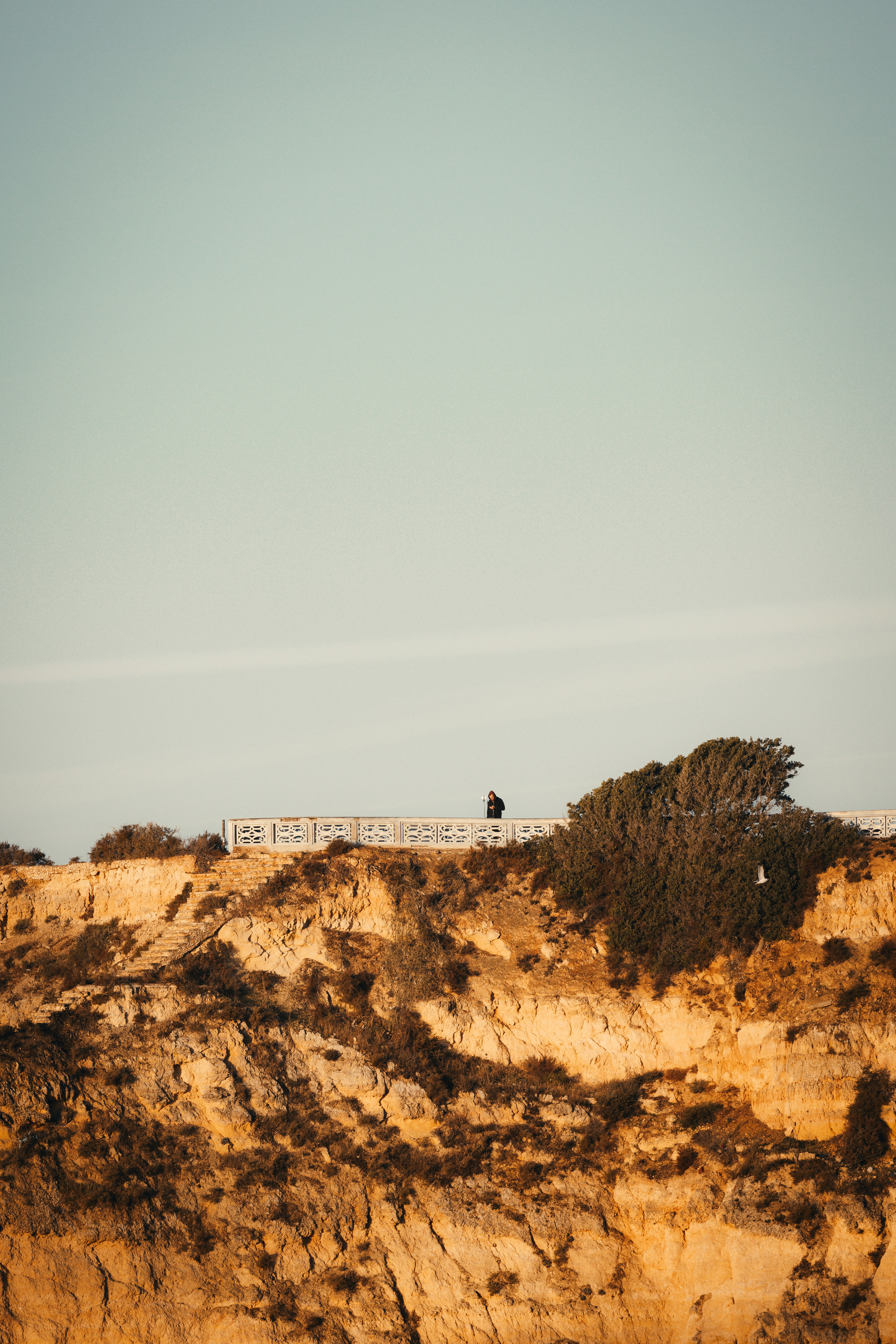 A lone figure walks along a cliffside path.