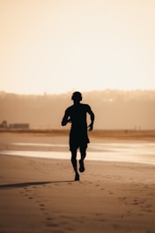 Silhouette of a man running on a beach at sunset.