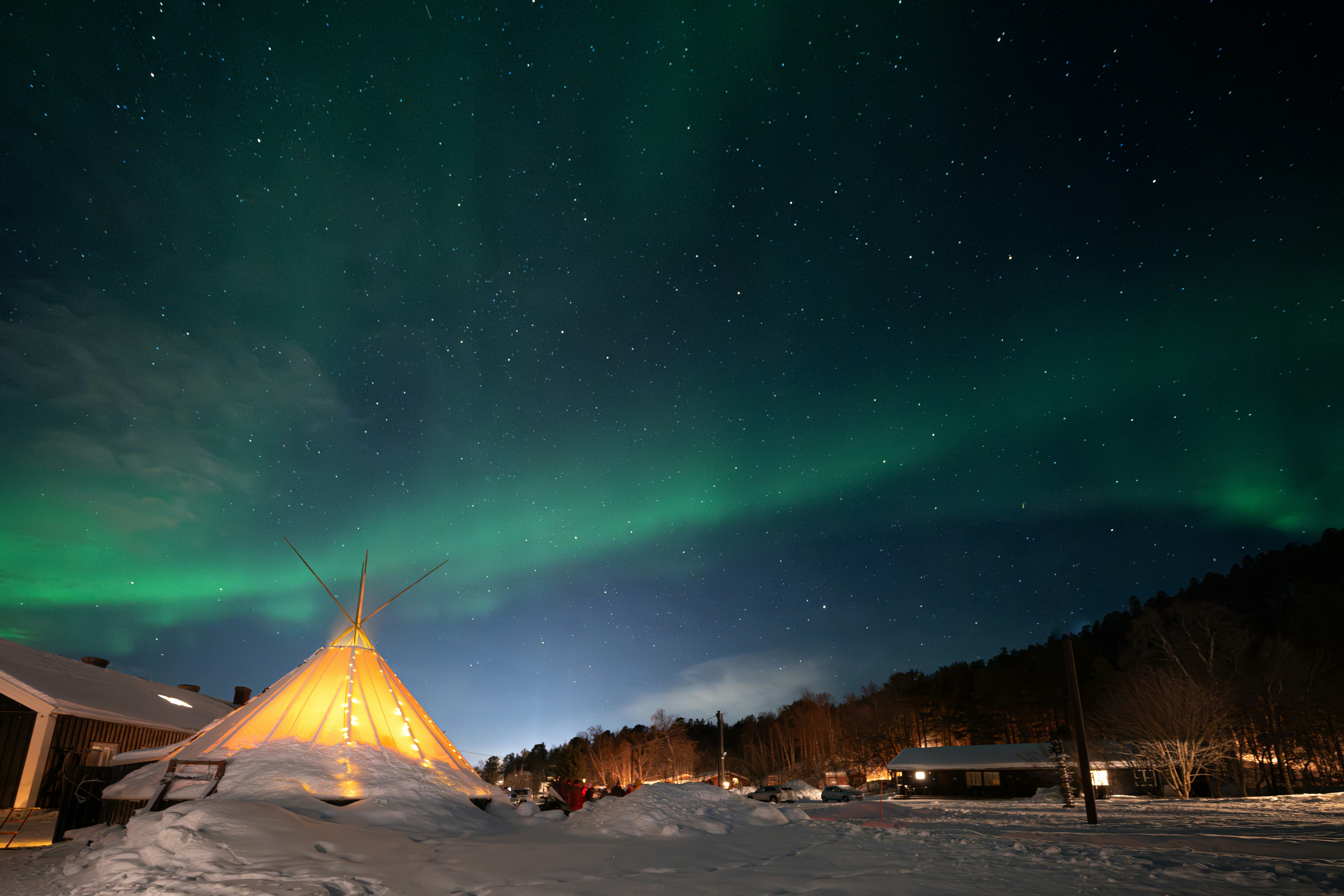 夜の雪に覆われた村の上にオーロラが輝いています