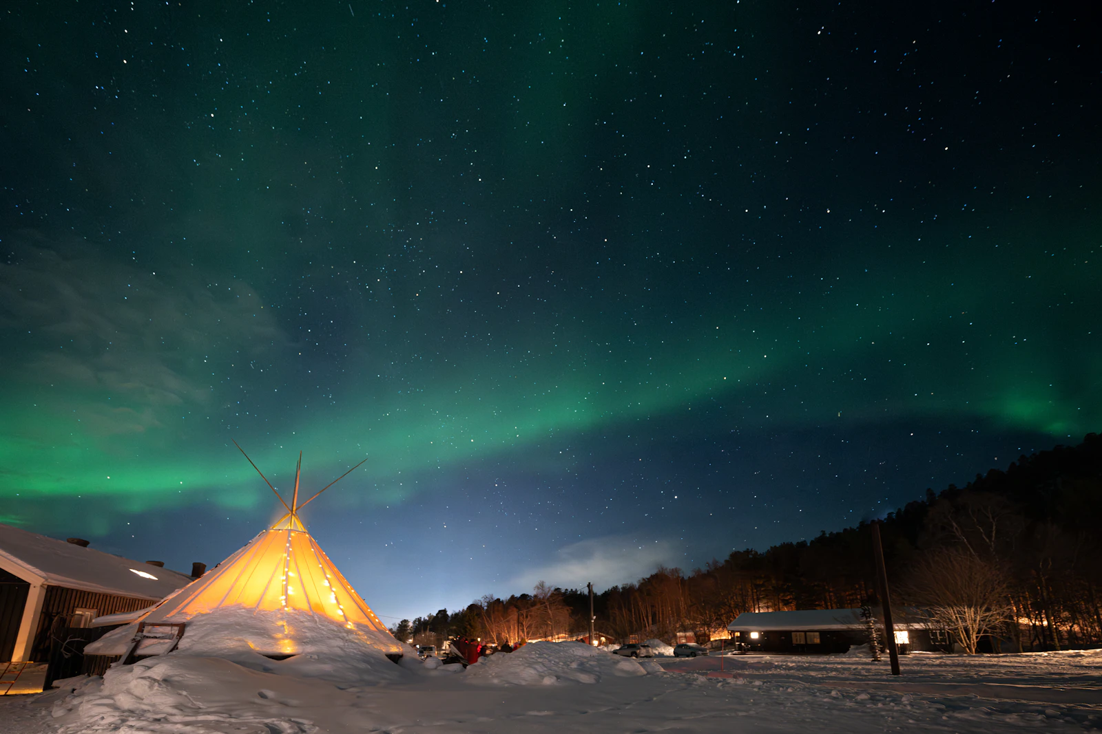 The aurora over a lit lavvu in the snow — Alta, Norway