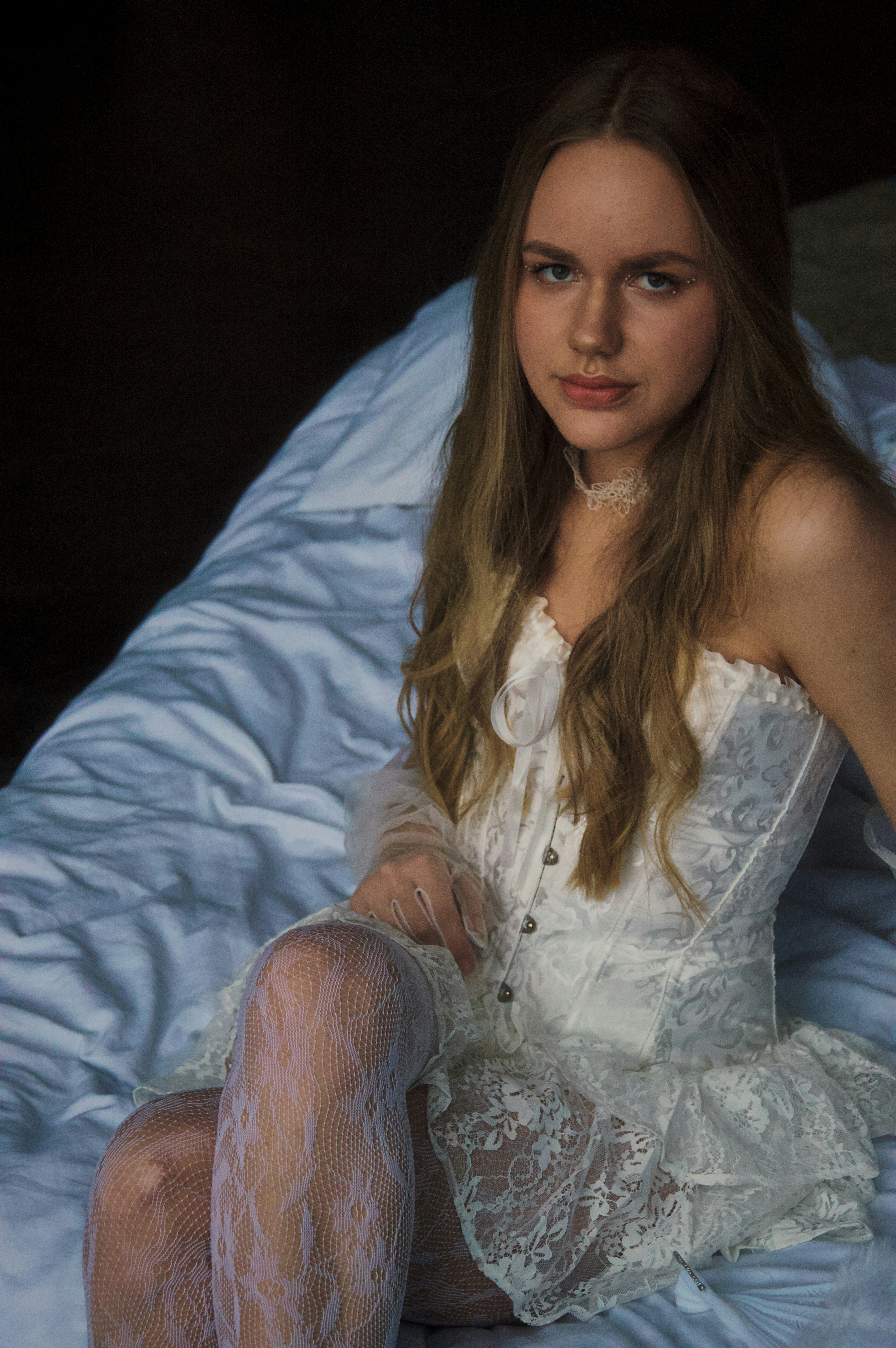 Young woman in white corset and lace stockings on bed