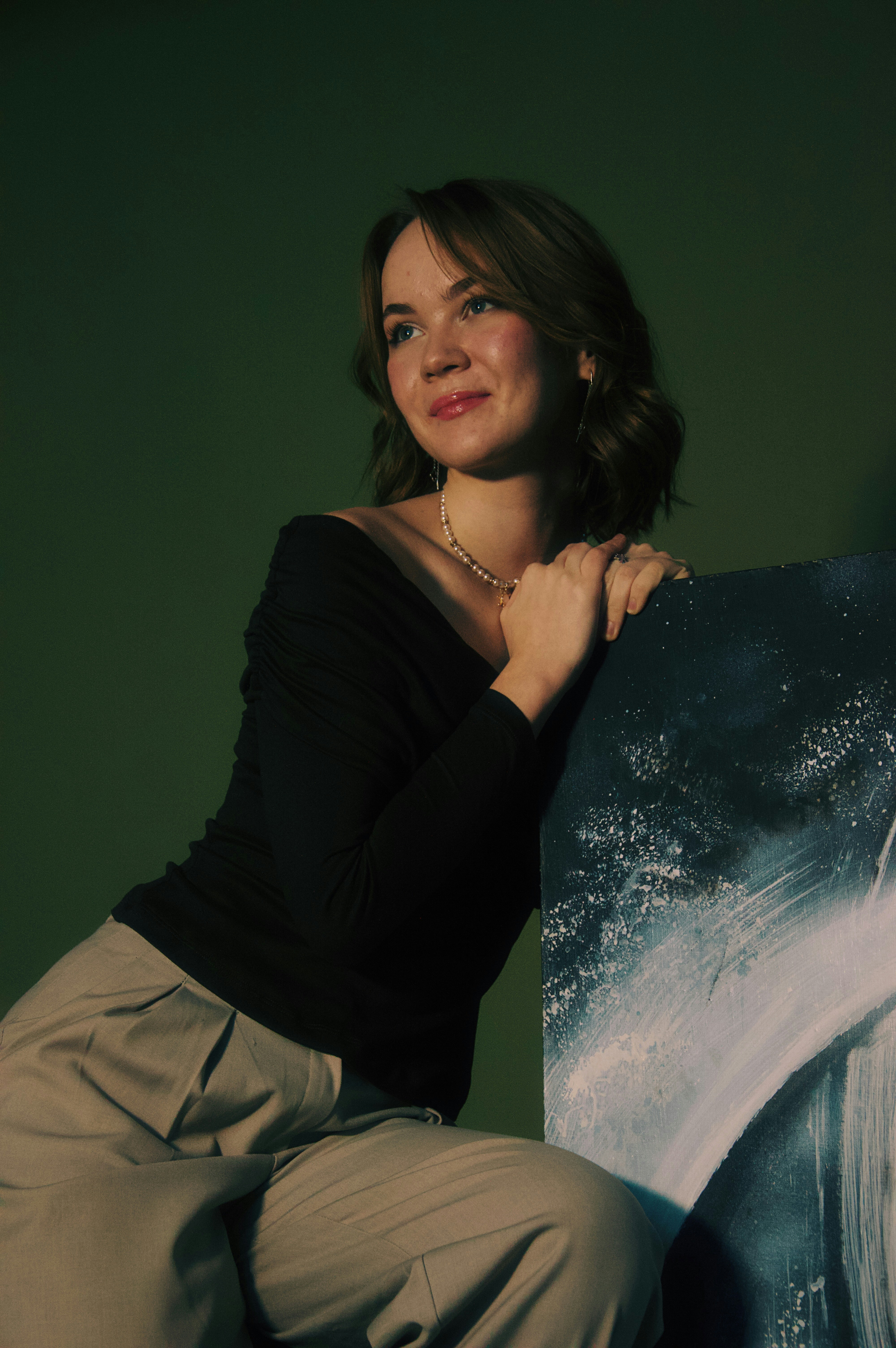 A young woman leans on abstract art against green background