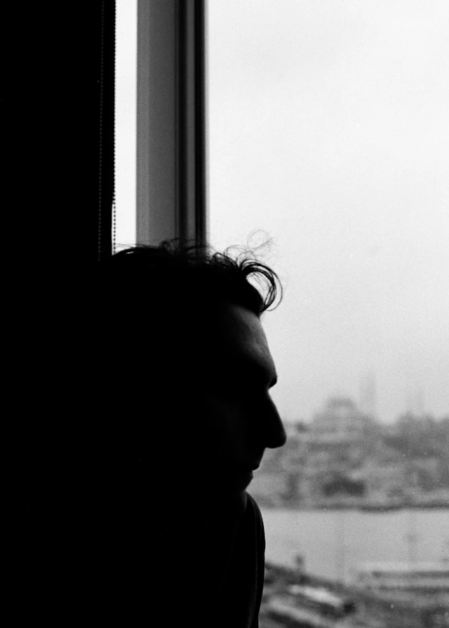 Silhouette of a man standing at a tall window, looking out over a city skyline
