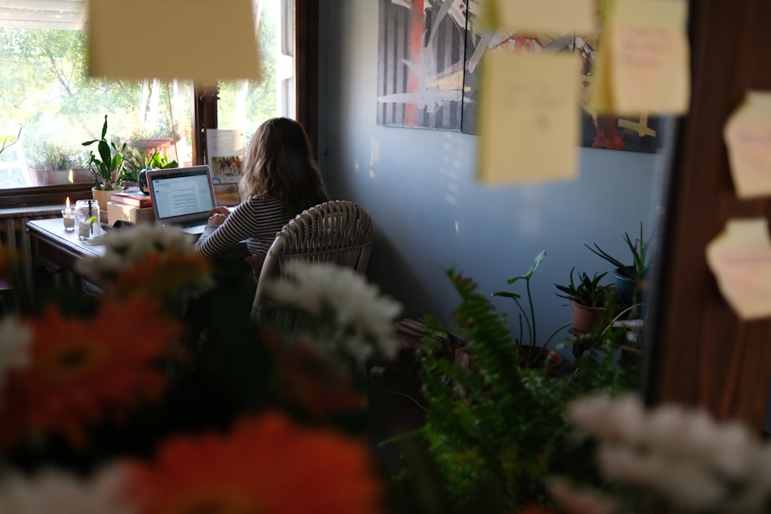Woman working on laptop at a desk with plants.