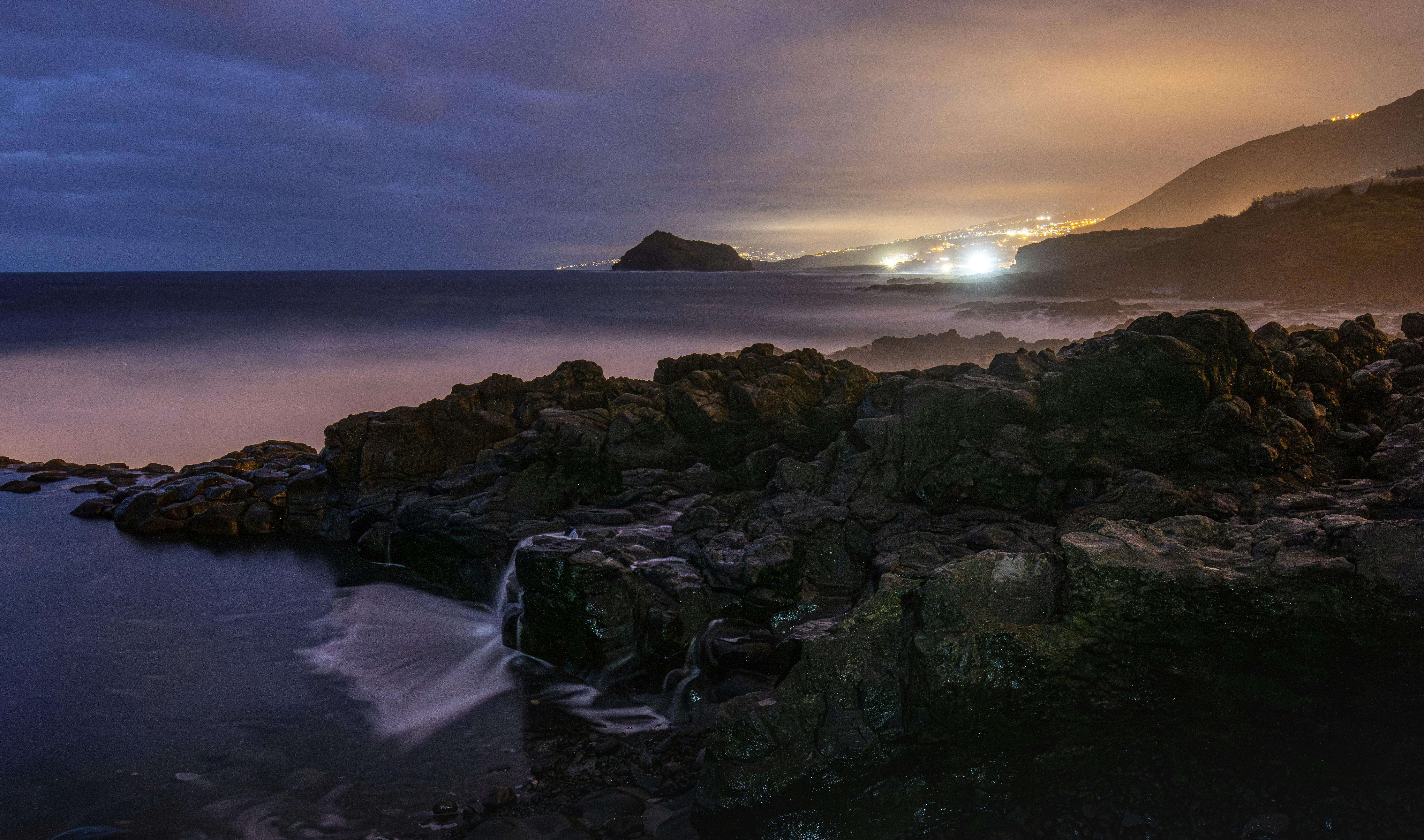 Rocky coastline with distant lights at dusk