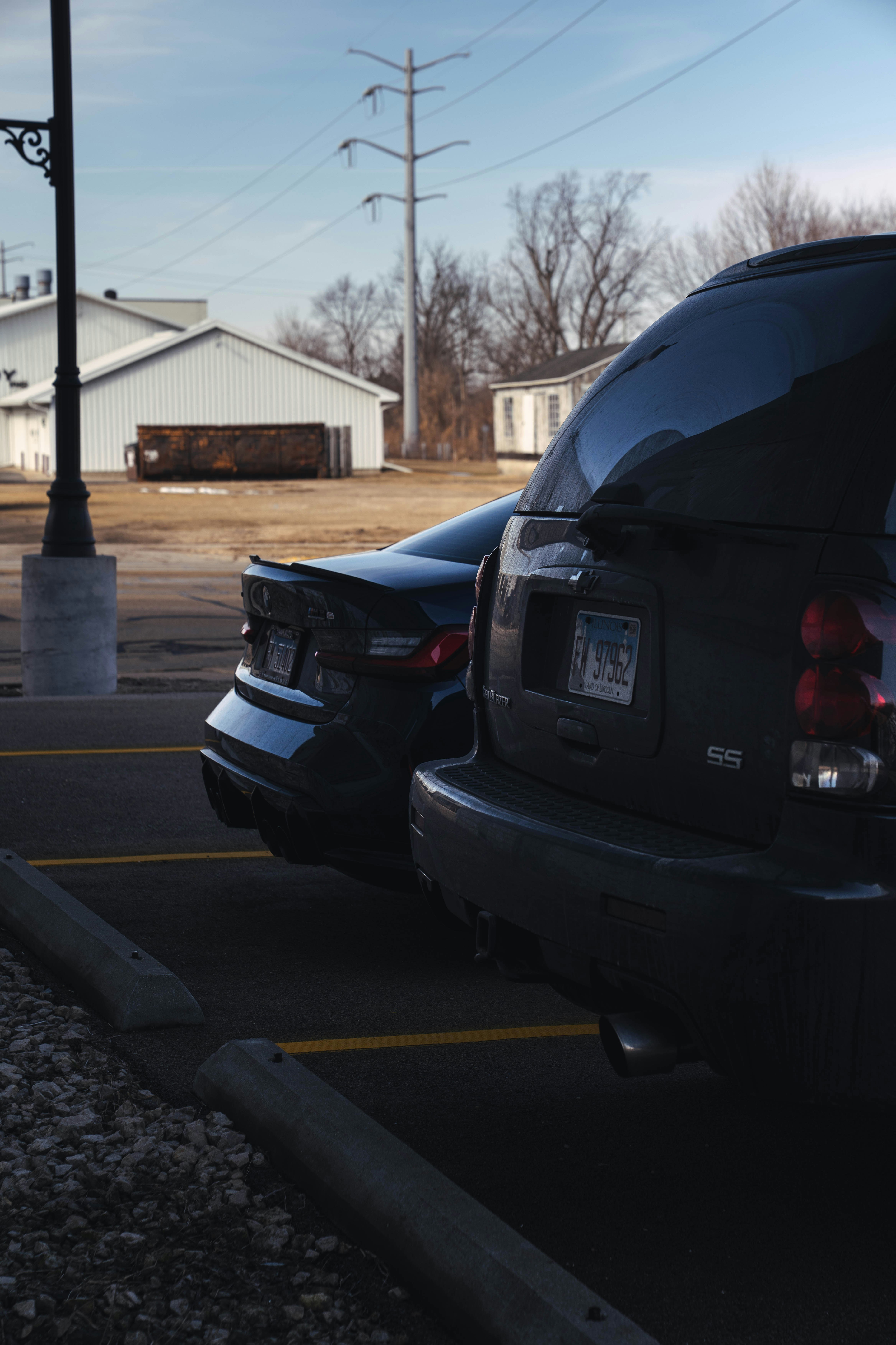 Two cars parked in a lot with buildings behind.