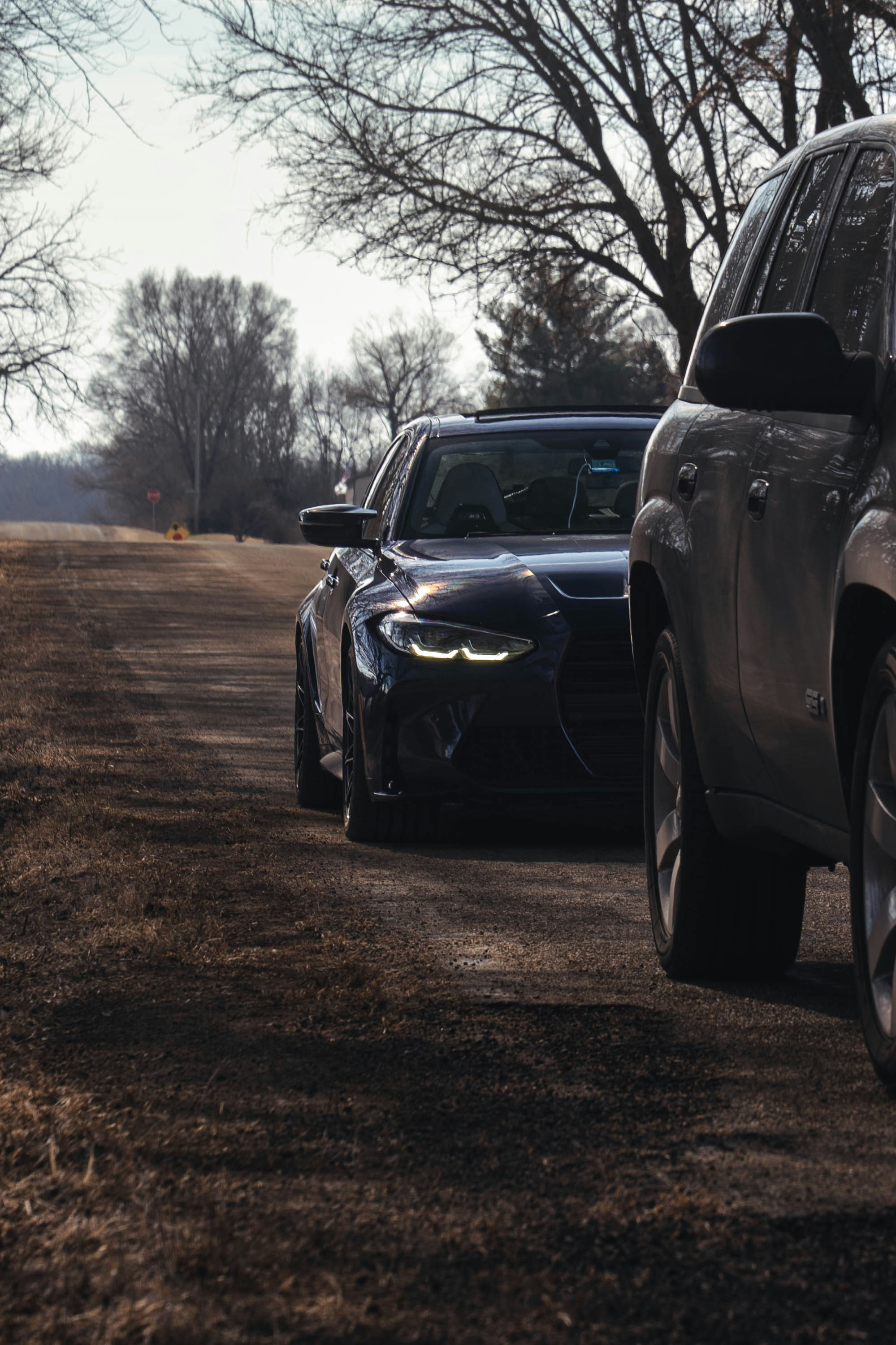 Two cars on a dirt road with bare trees