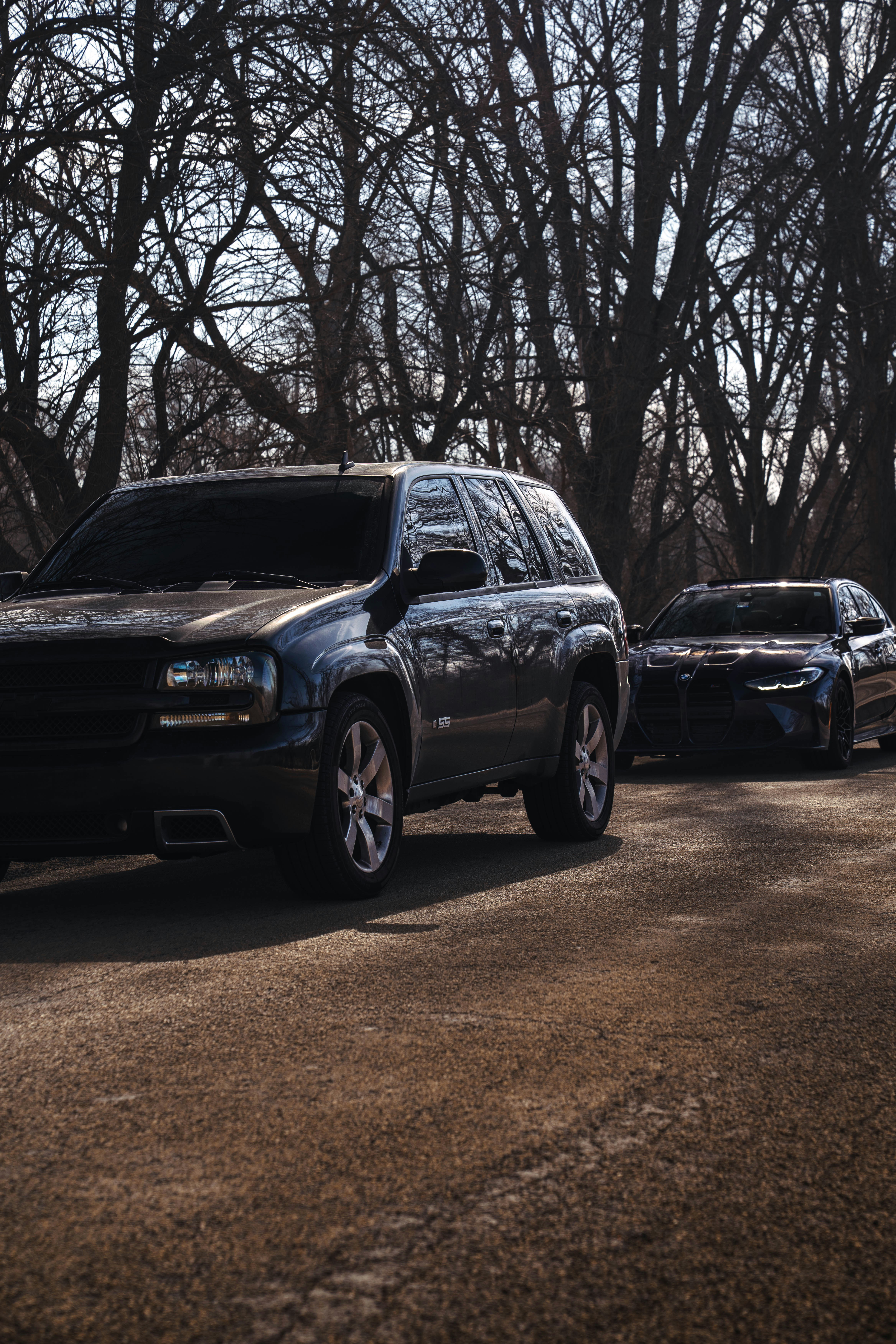 Two cars parked on a dirt road with trees.