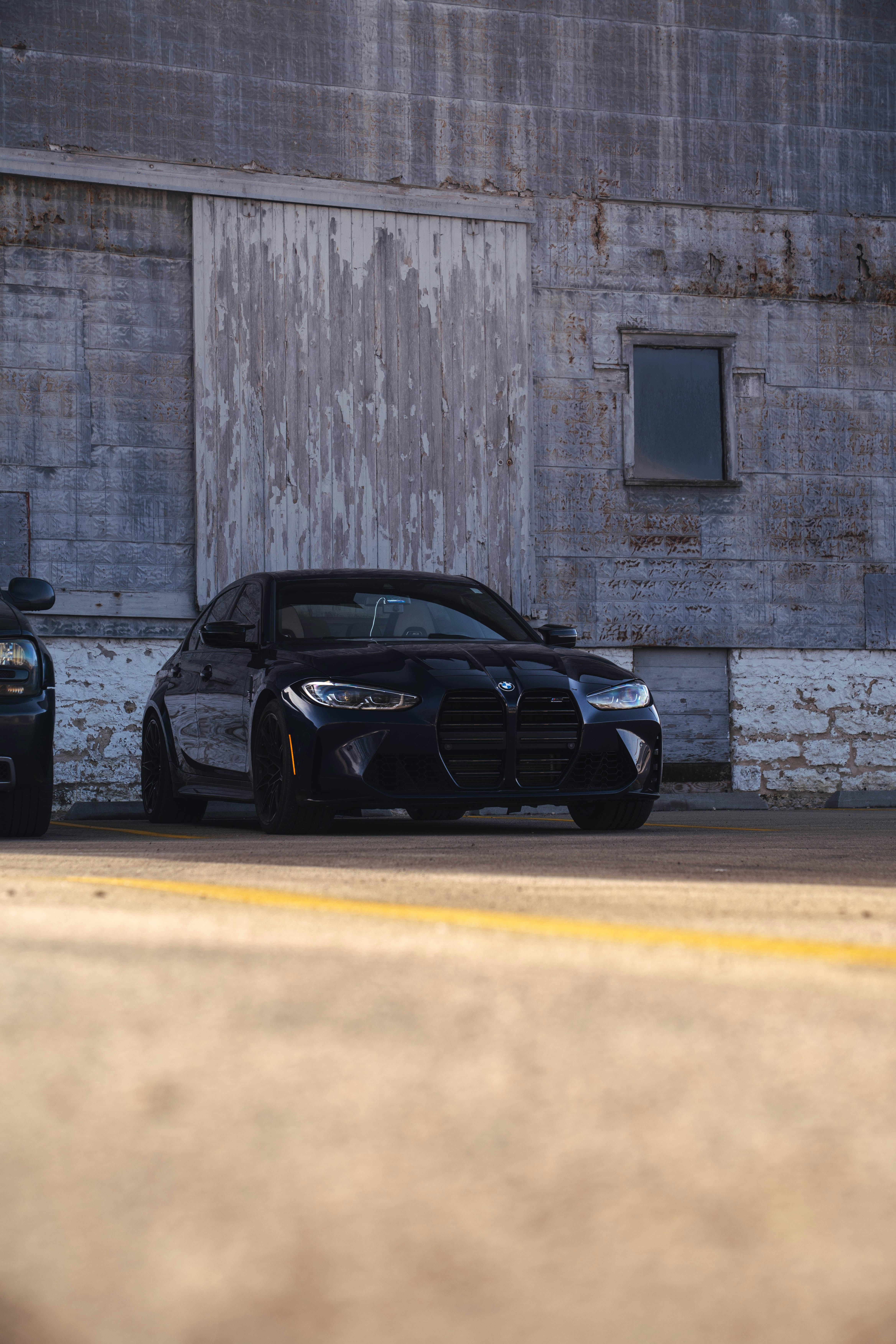 A sleek black car parked outside a weathered building.