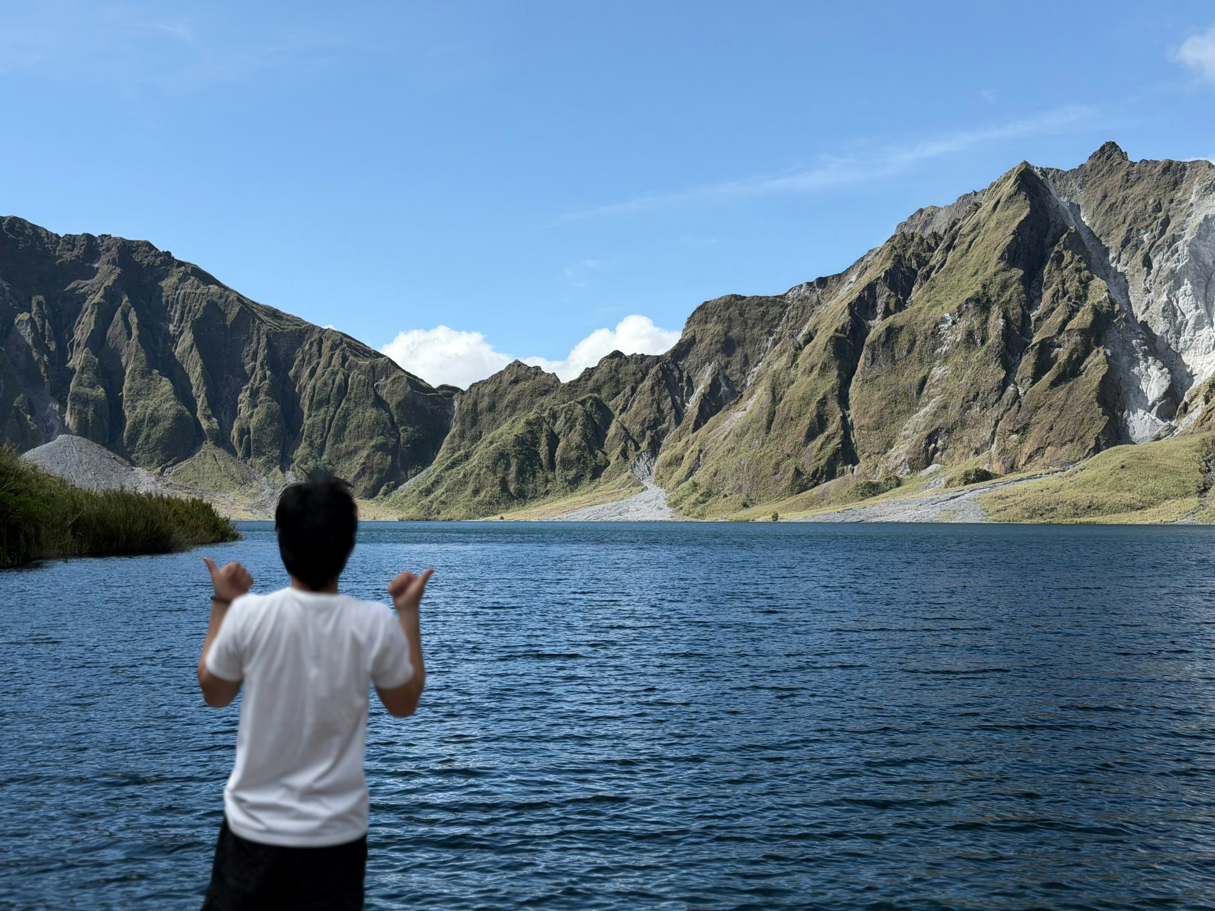 Person standing by a blue lake with mountains