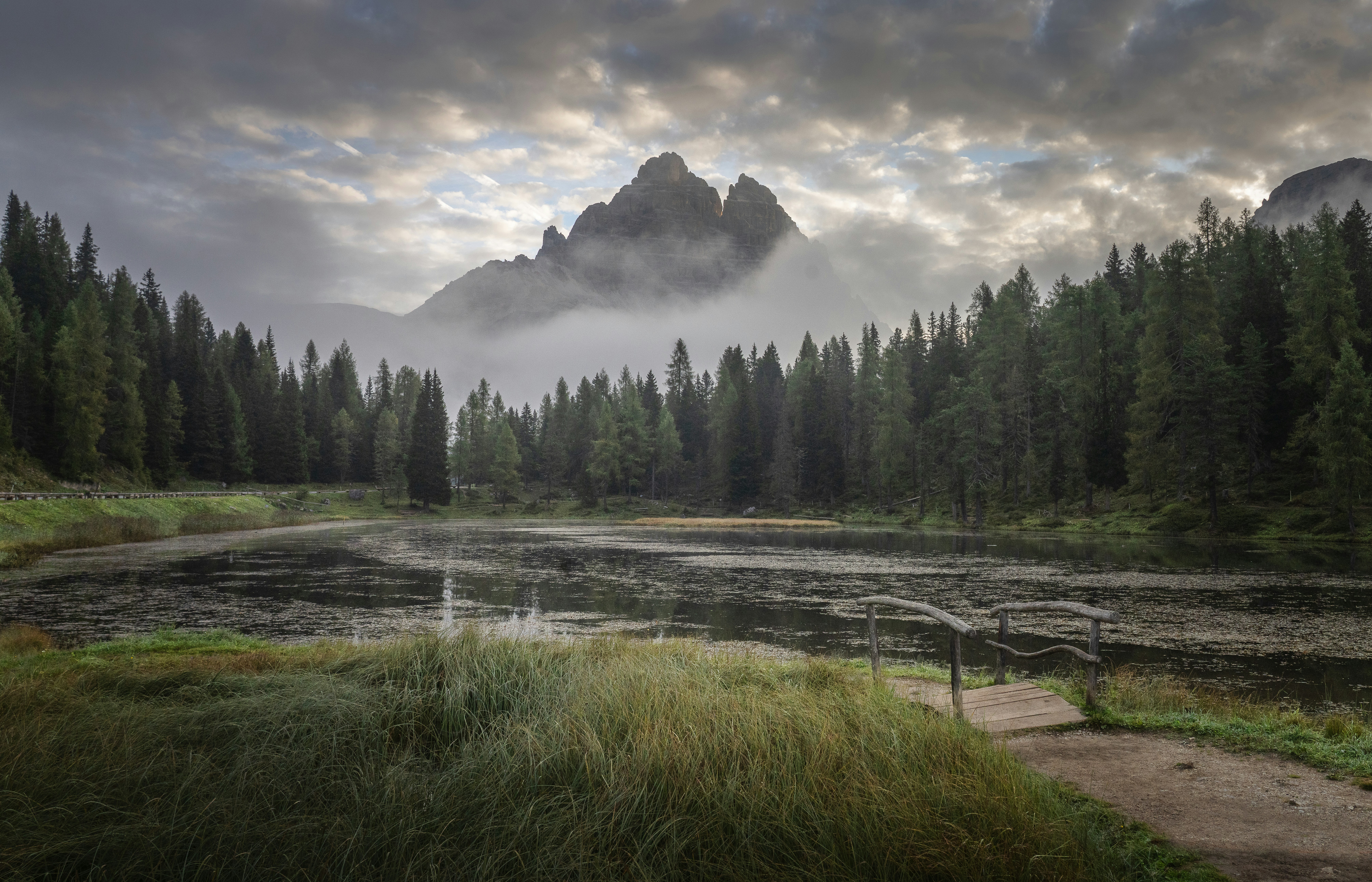 Des montagnes brumeuses s’élèvent au-dessus d’une forêt et d’un lac paisibles.