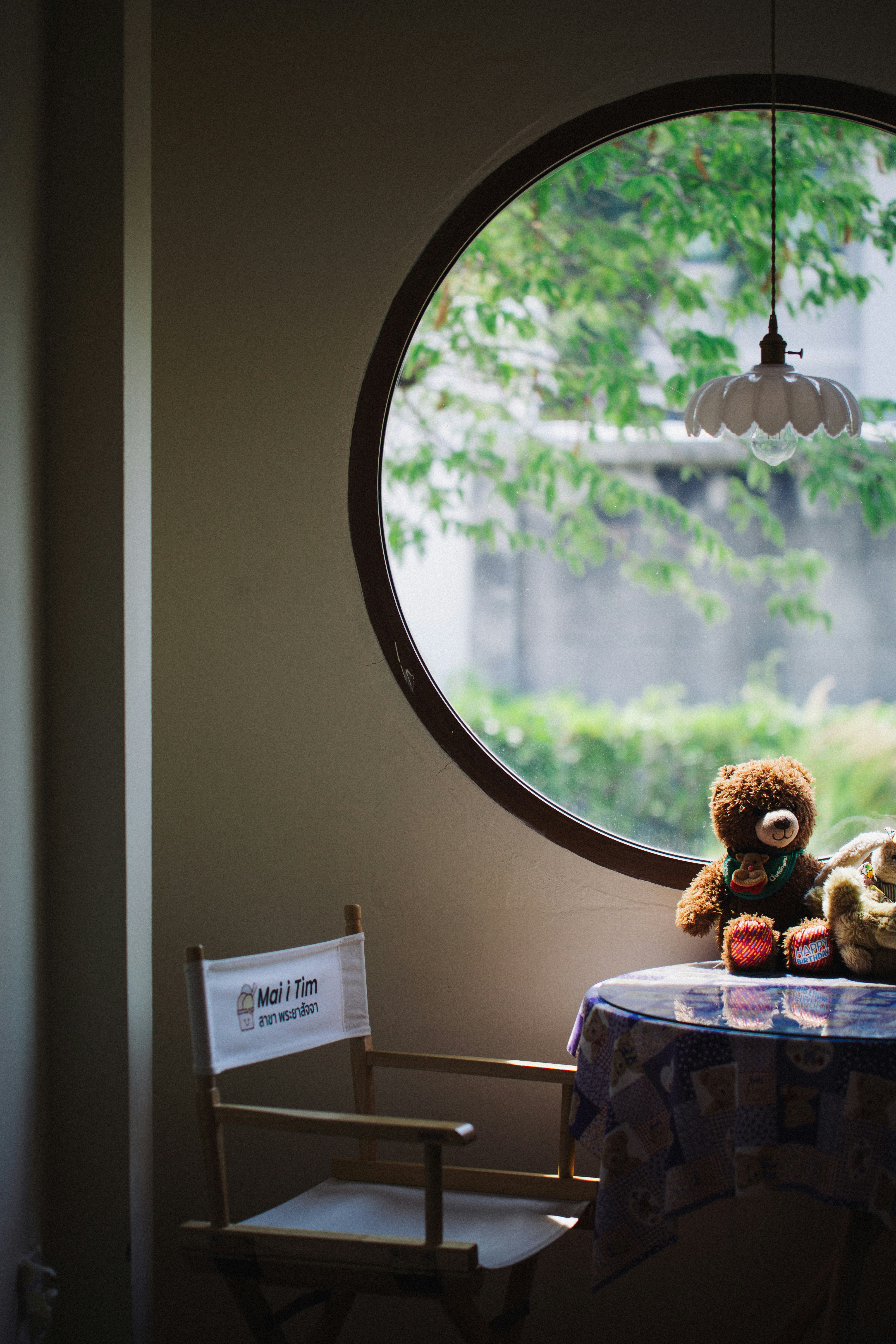 Teddy bears sit on a table by a round window.