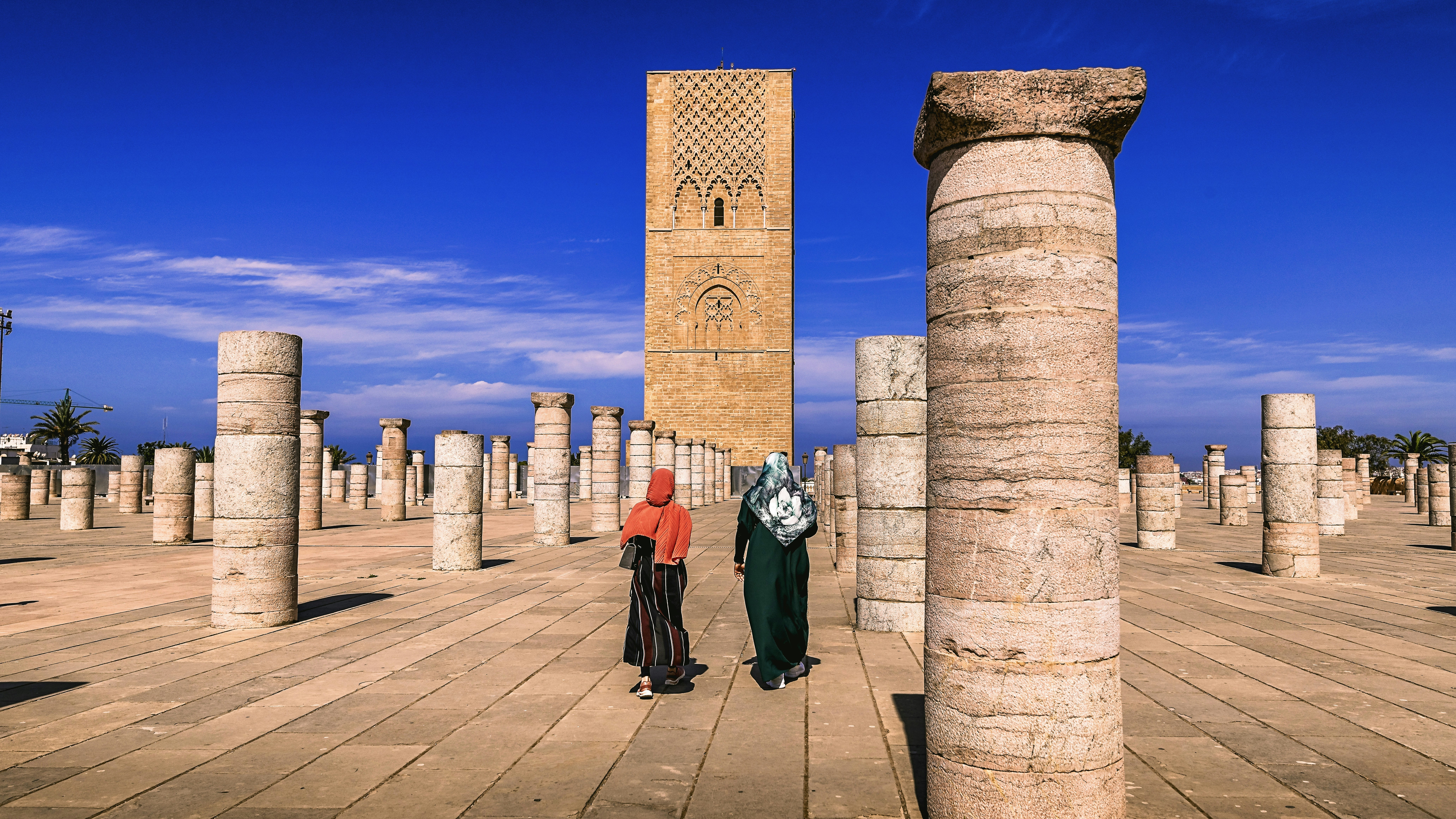Two people walk through ancient ruins with tower