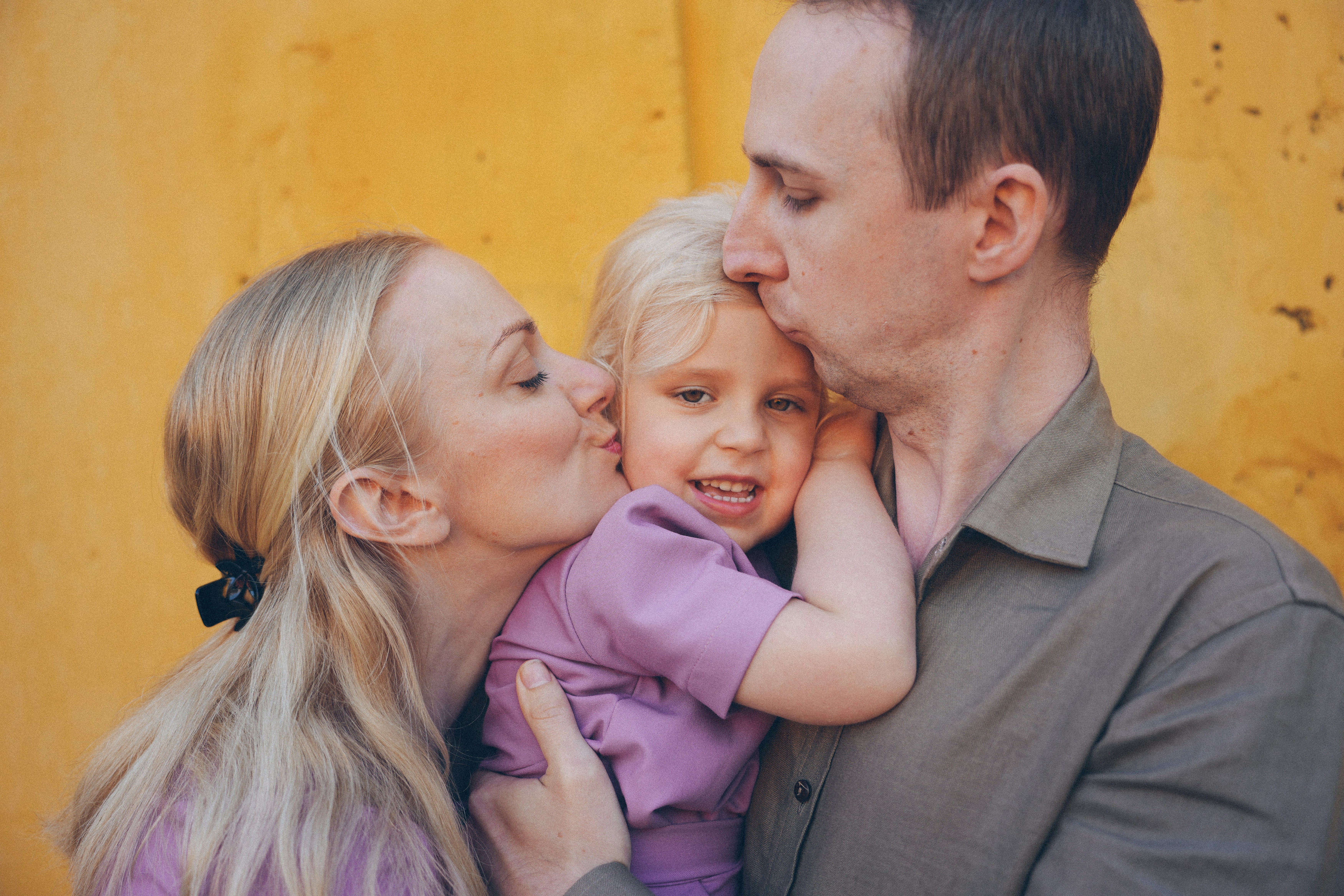 Eltern, die ihre Tochter auf die Stirn küssen.