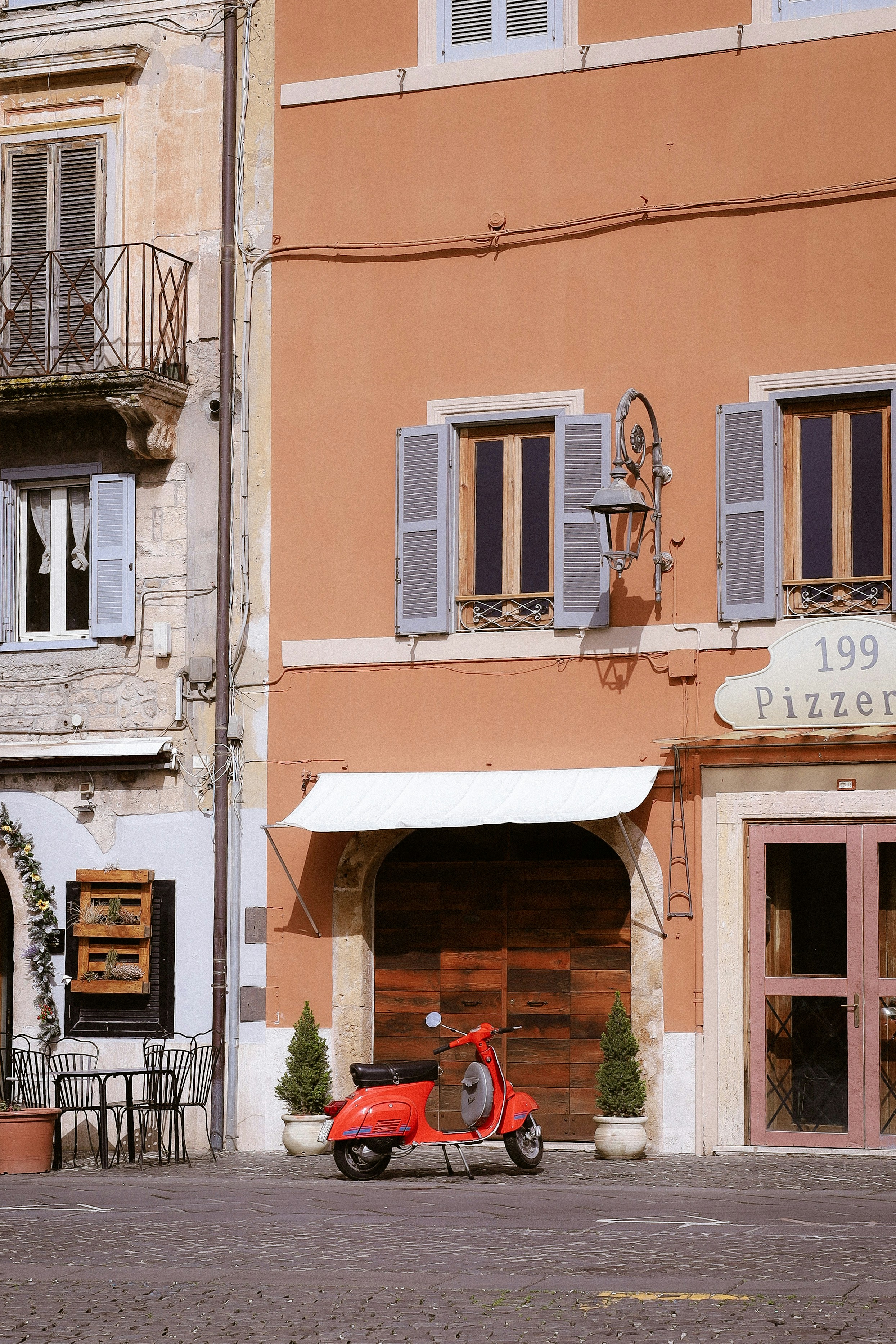 Scooter rojo aparcado fuera de una pizzería con edificio italiano.