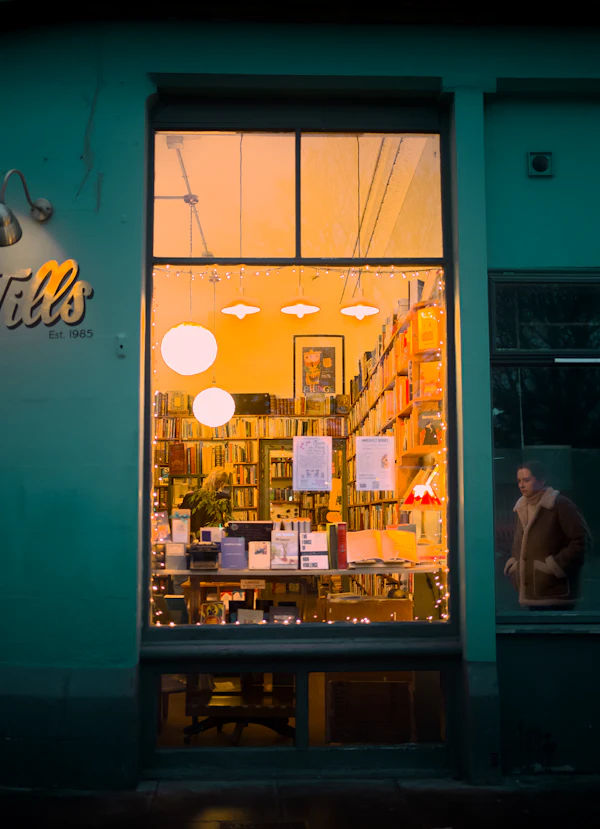 A warmly lit bookshop window display at night showing stacked books