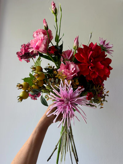 Hand holding a vibrant bouquet of assorted flowers.