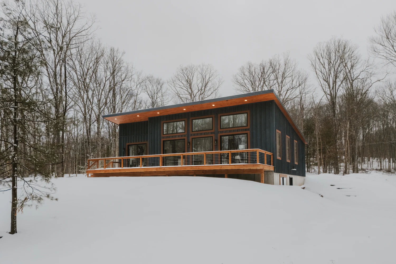 Dark-clad timber house with a wide deck on a snowy slope