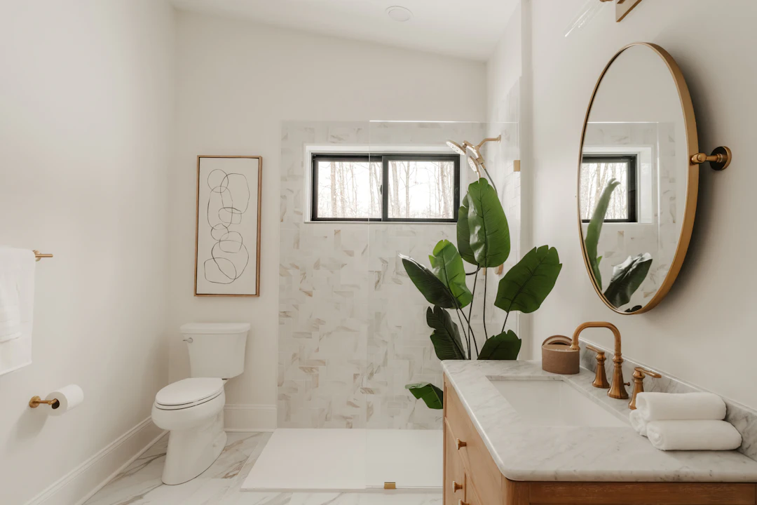 Spotless bathroom with a marble shower, wood vanity, round mirror and a large plant