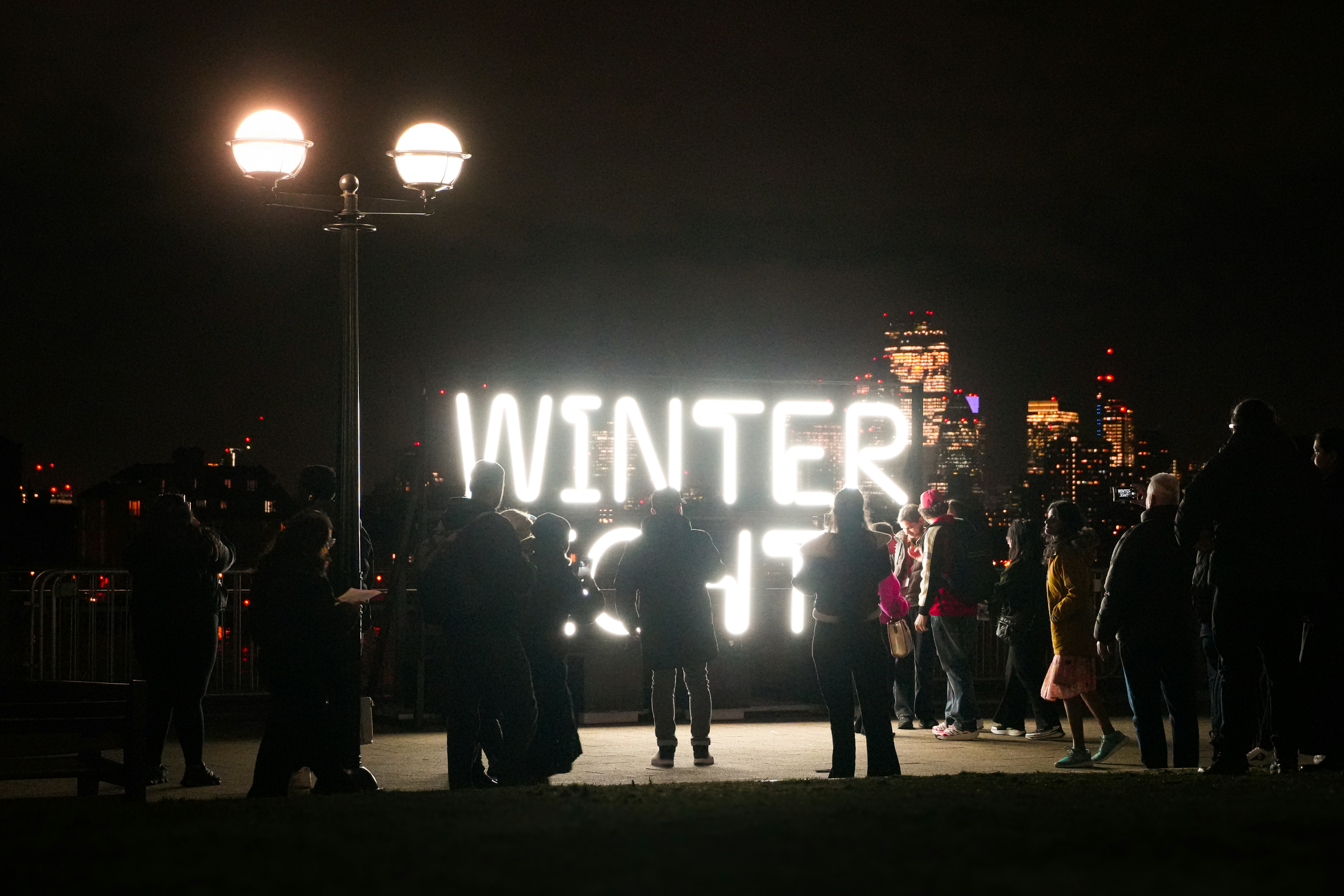 People gather at night near a large illuminated "winter" sign.