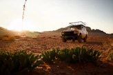 A rugged suv parked in a desert Karoo landscape at sunset.