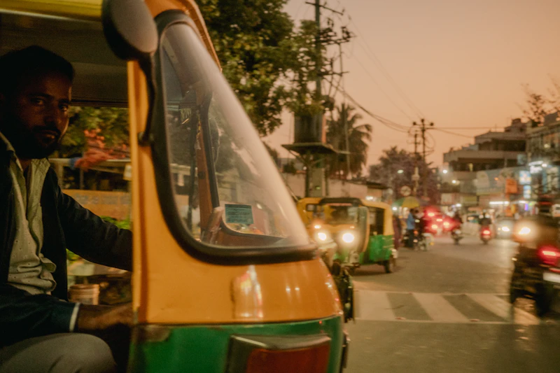 Indian tuk-tuk driver in bustling traffic at dusk