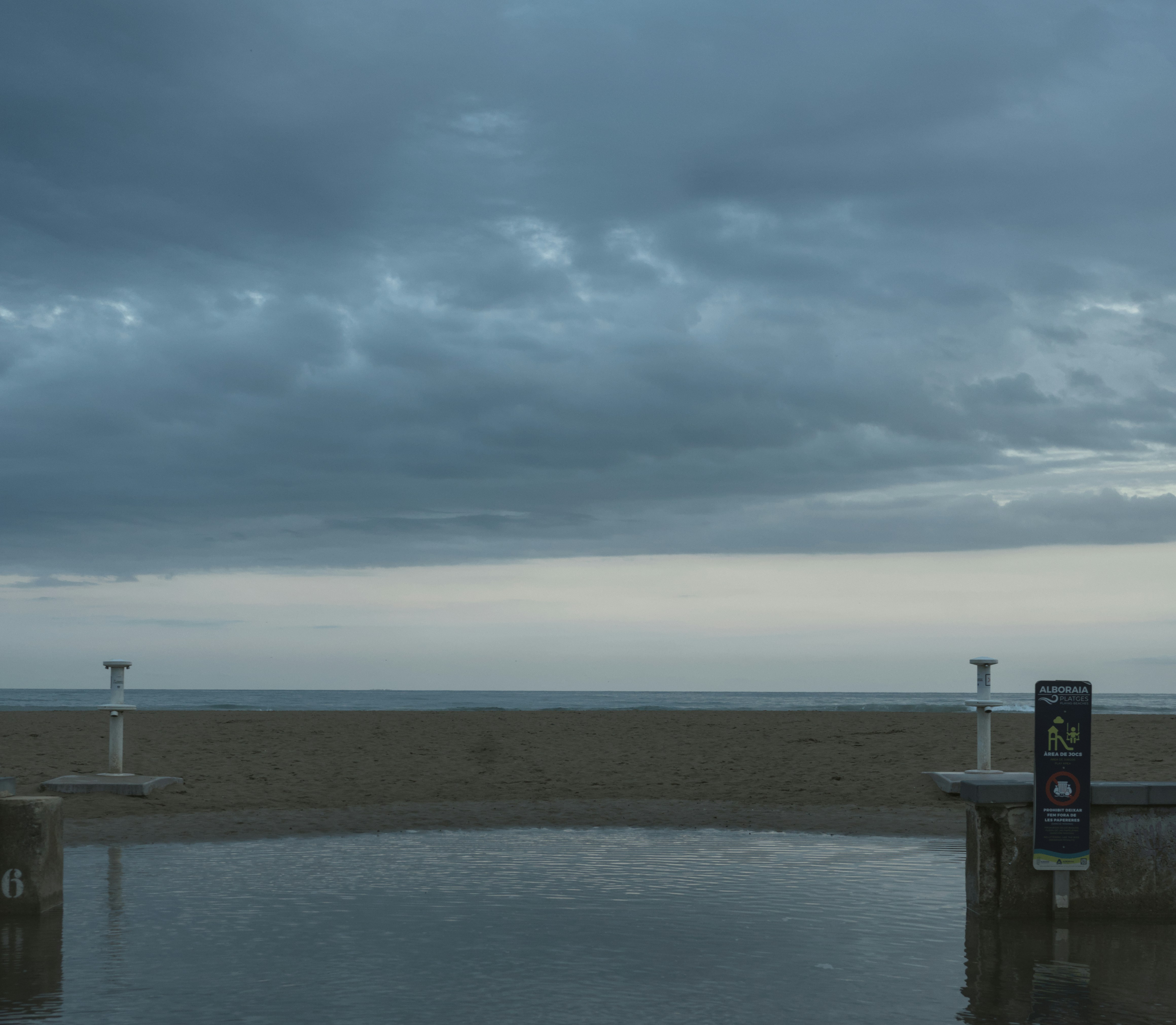 A calm beach with cloudy skies and a reflecting pool.