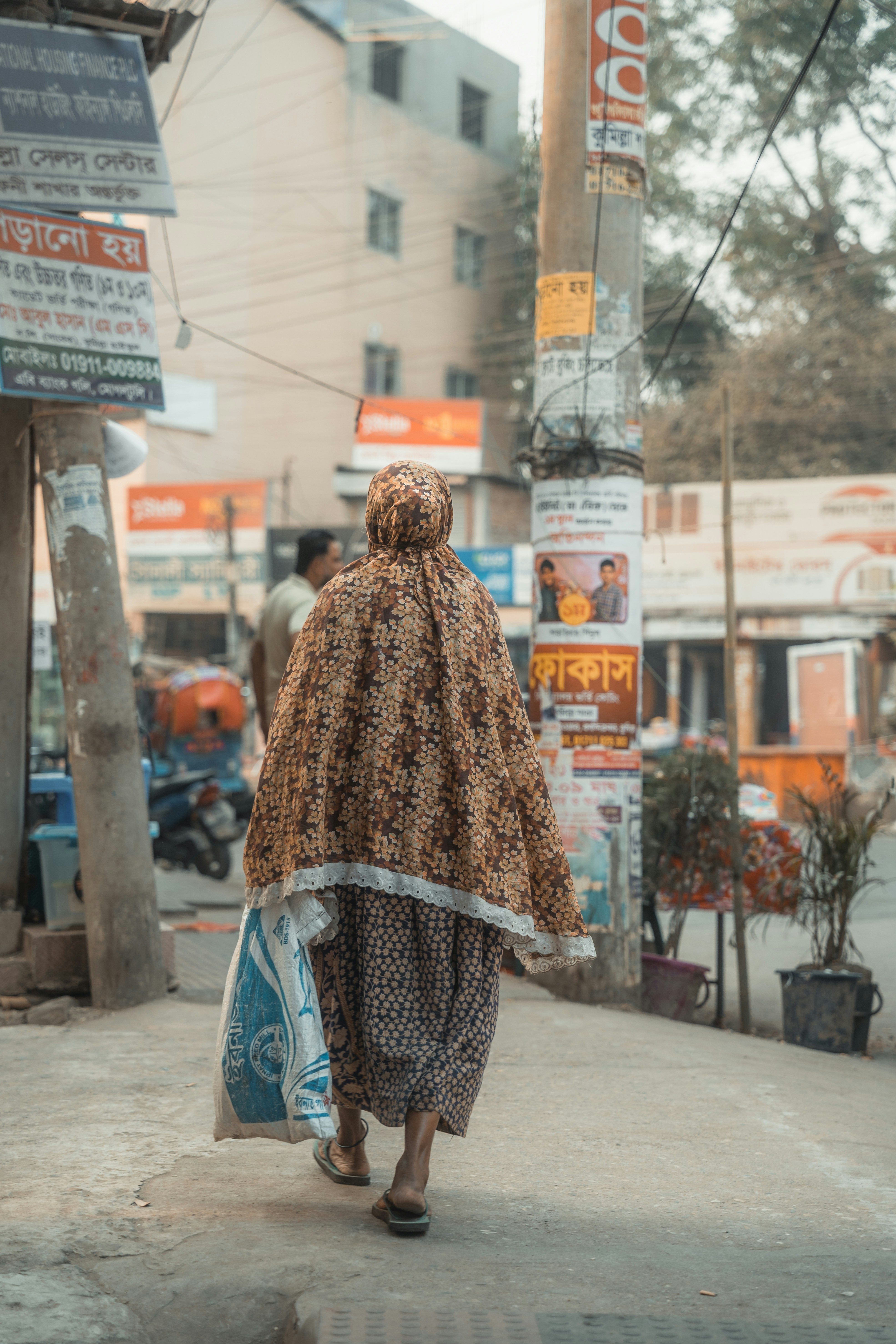Frau, die eine Straße entlanggeht und eine Tasche trägt.