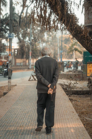Elderly man walks down a sidewalk with hands clasped
