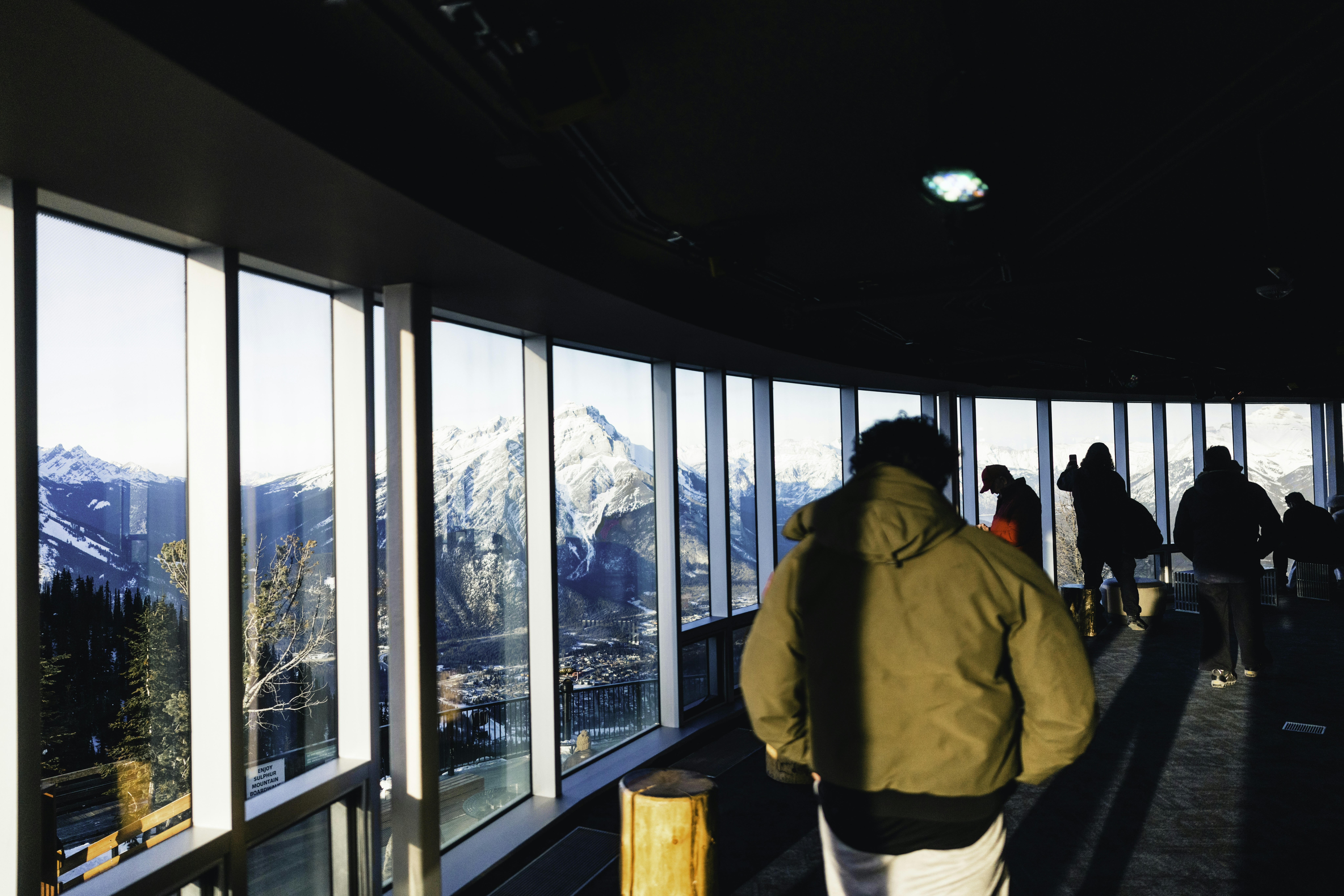 People walk past large windows with mountain views.