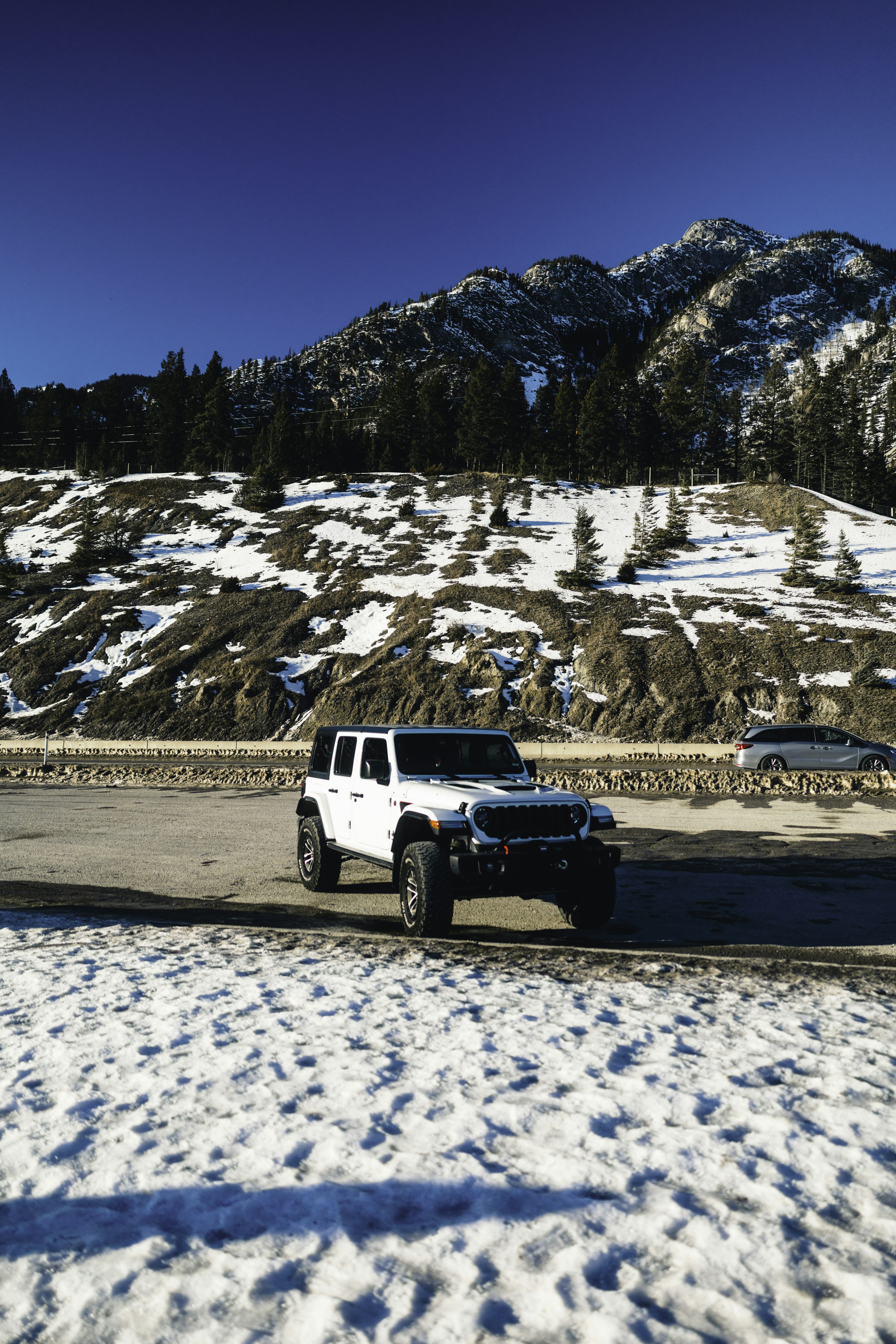 White jeep parked on snowy road with mountains behind