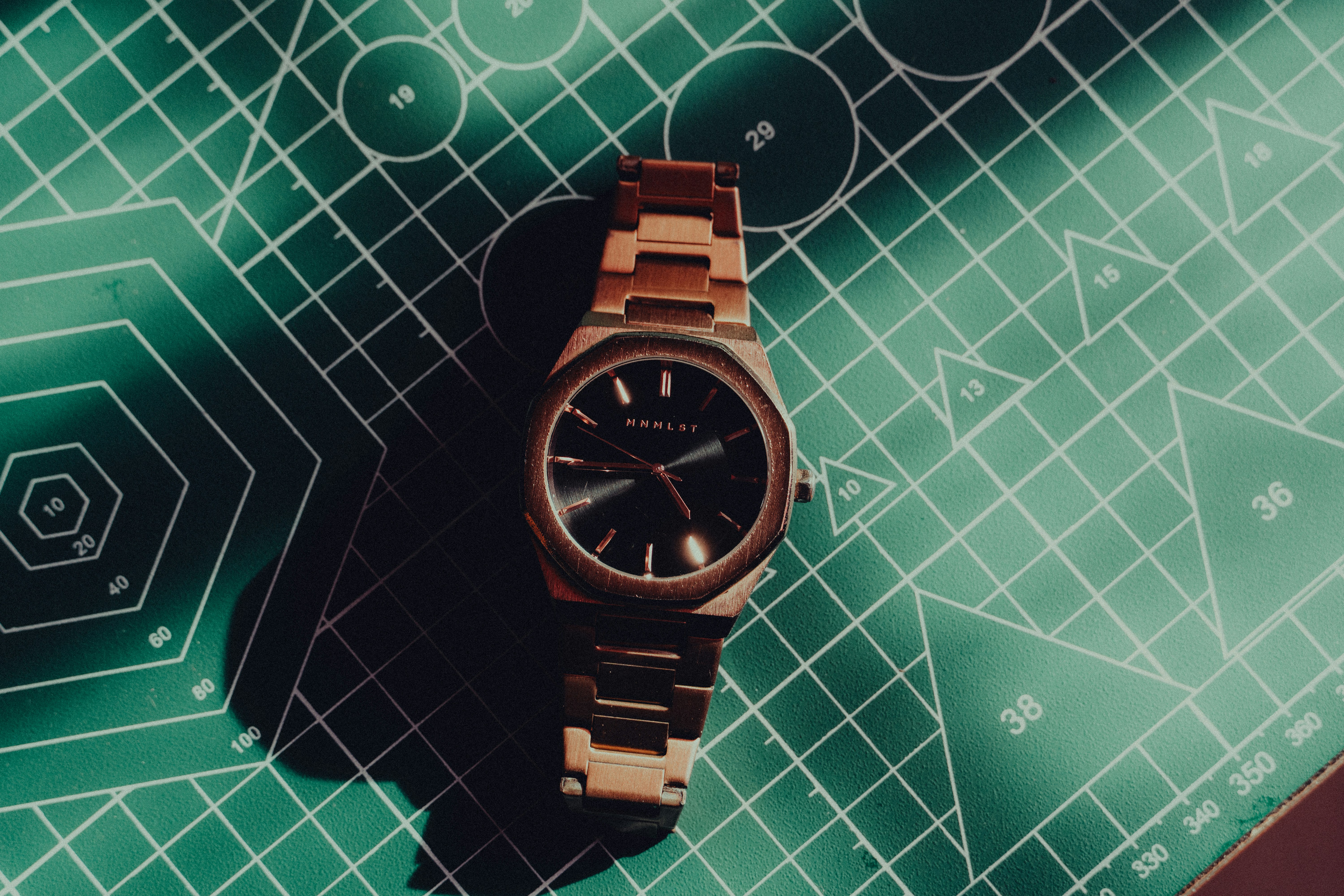 Un orologio in oro rosa poggia su uno sfondo a griglia verde.