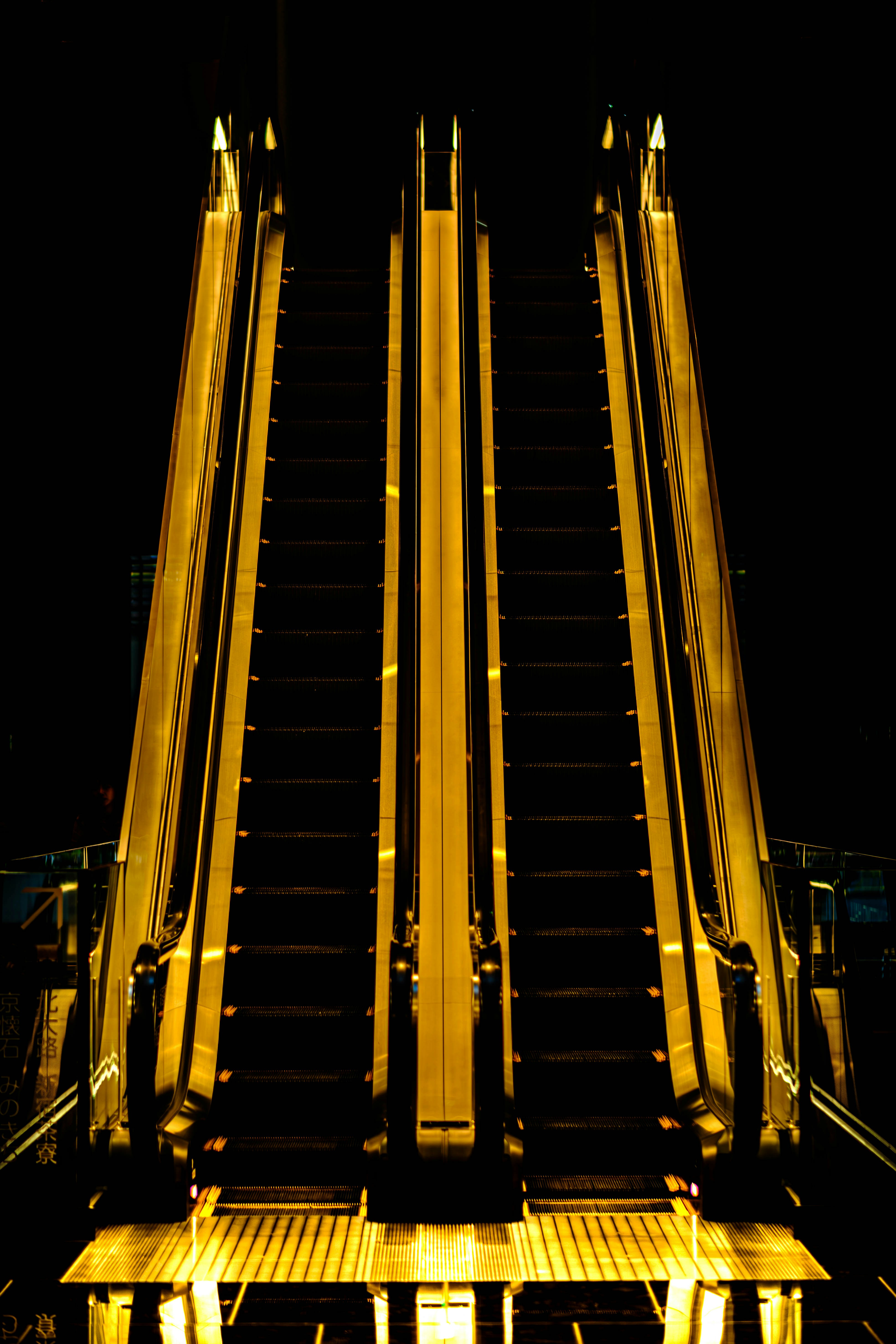 Three illuminated escalators ascend into darkness