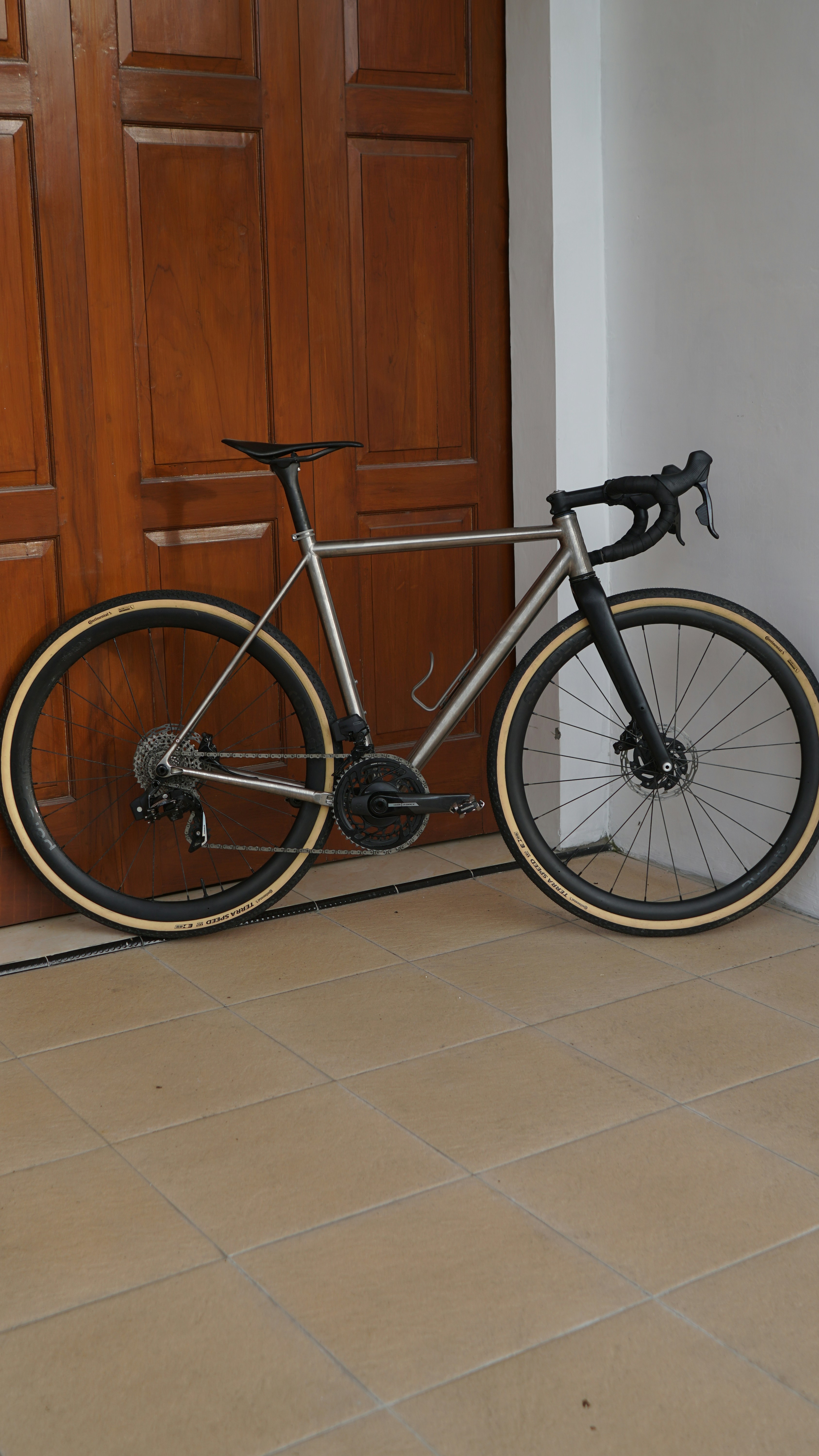 A silver gravel bike leans against a wooden door.