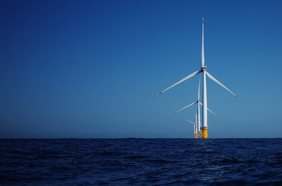 Large white wind turbine with three blades floats on ocean's surface near island