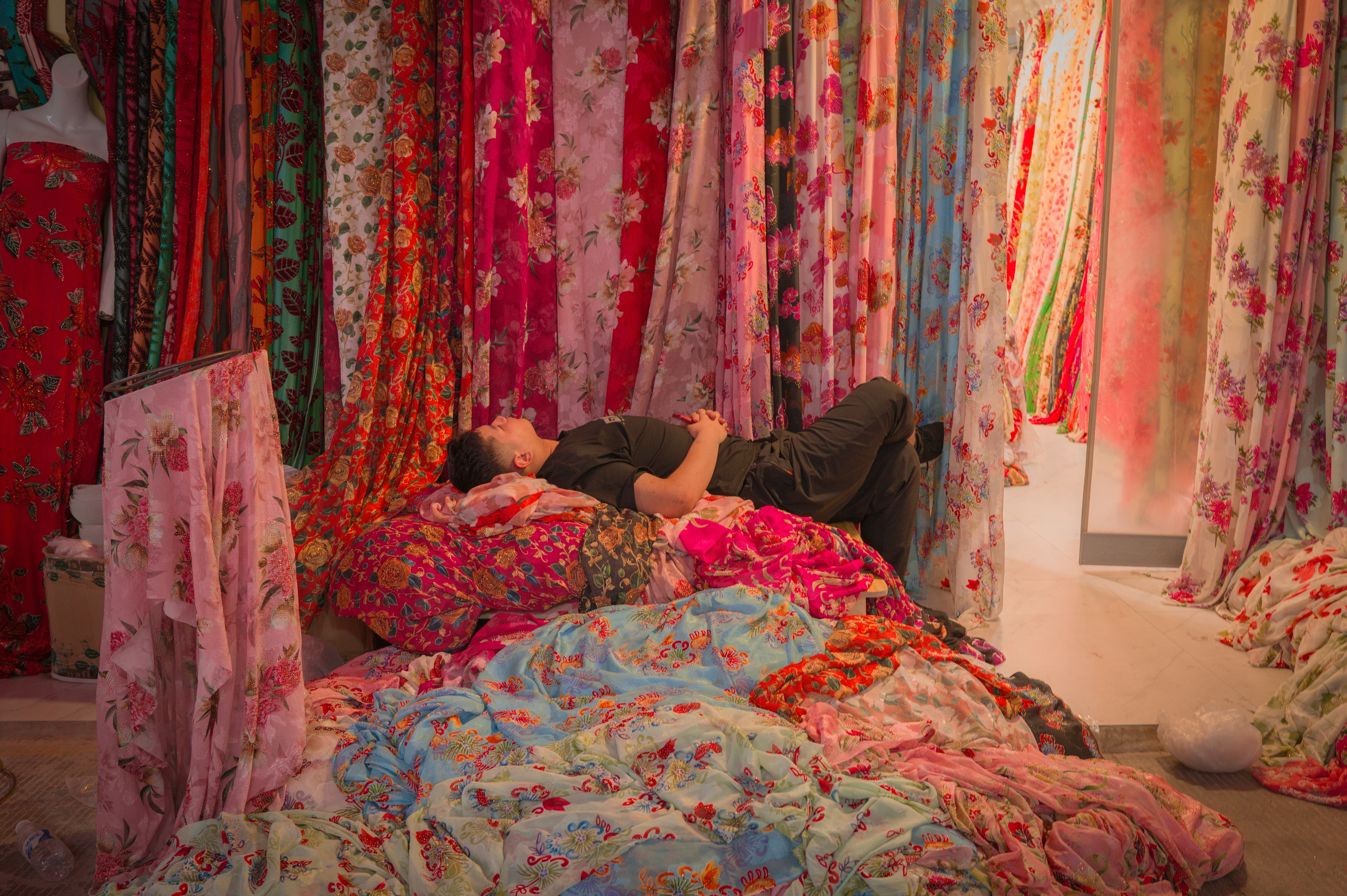 A person rests among piles of colorful floral fabric.