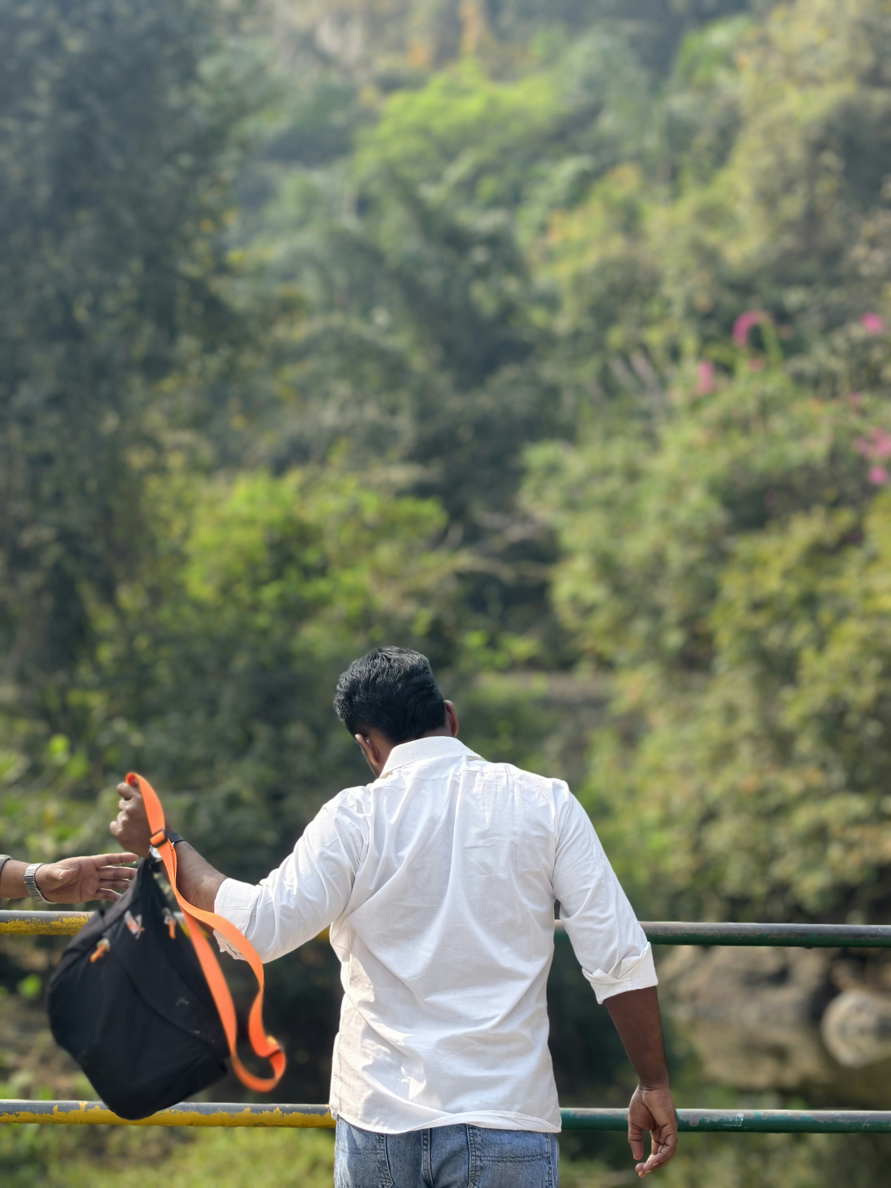 Man in white shirt holding a bag with orange straps.