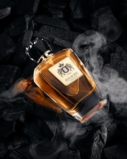 Perfume bottle surrounded by dark charcoal and smoke