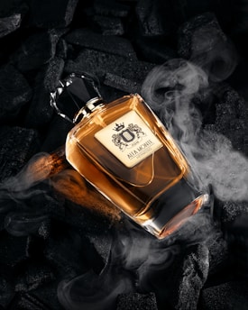 Perfume bottle surrounded by dark charcoal and smoke