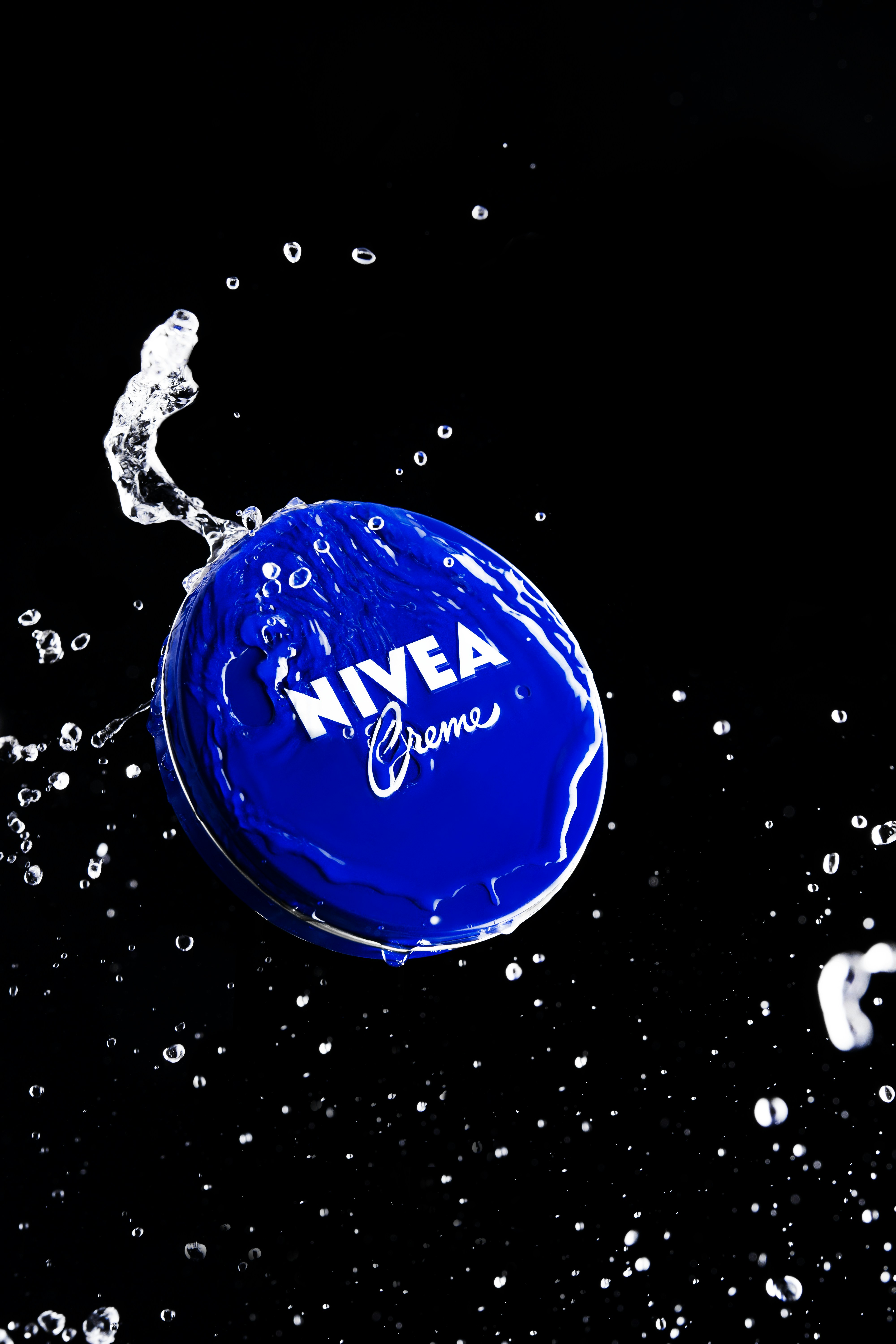 Nivea-Crème-Dose mit Wasser spritzt auf schwarzem Hintergrund