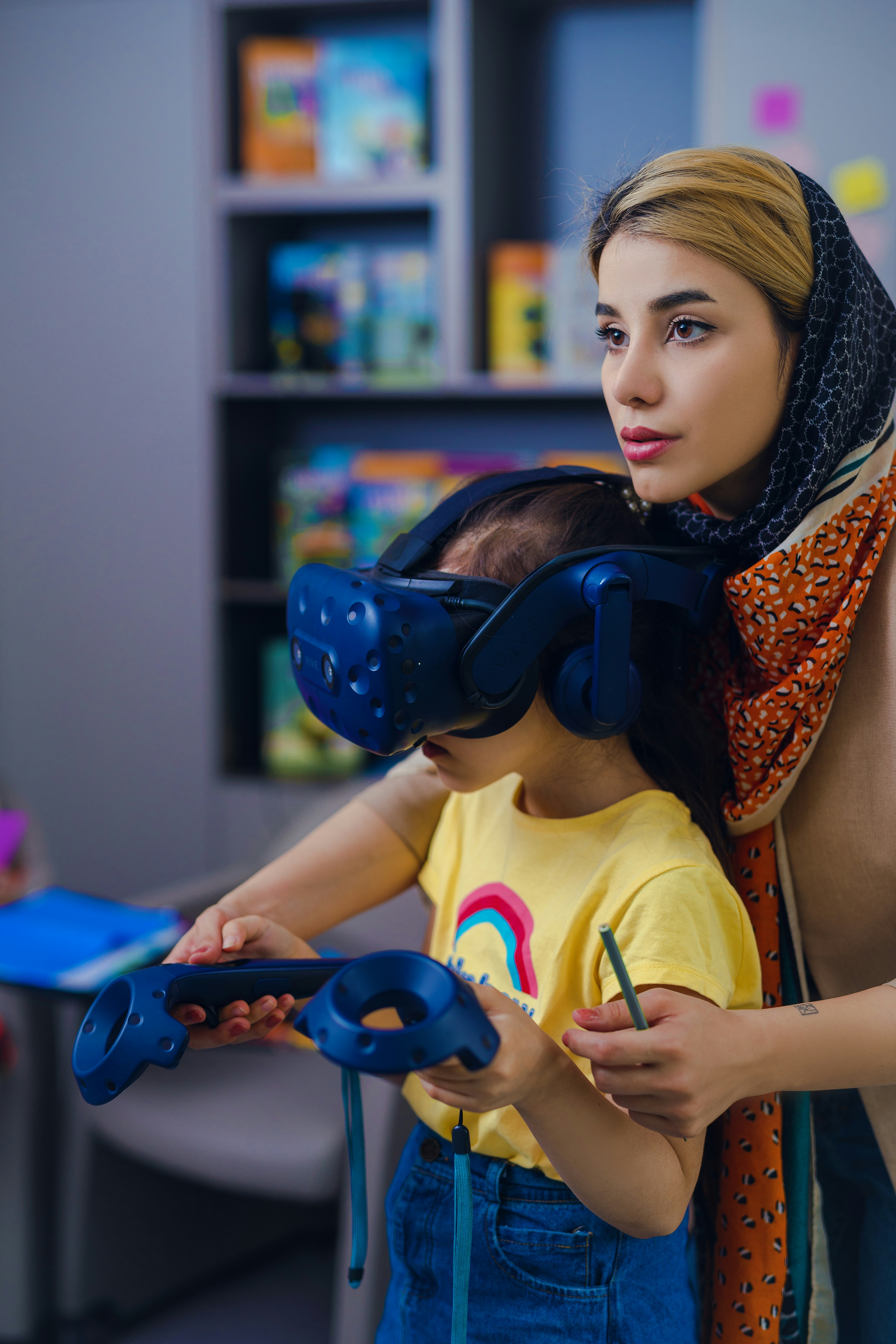 Woman helps child use virtual reality headset and controllers.