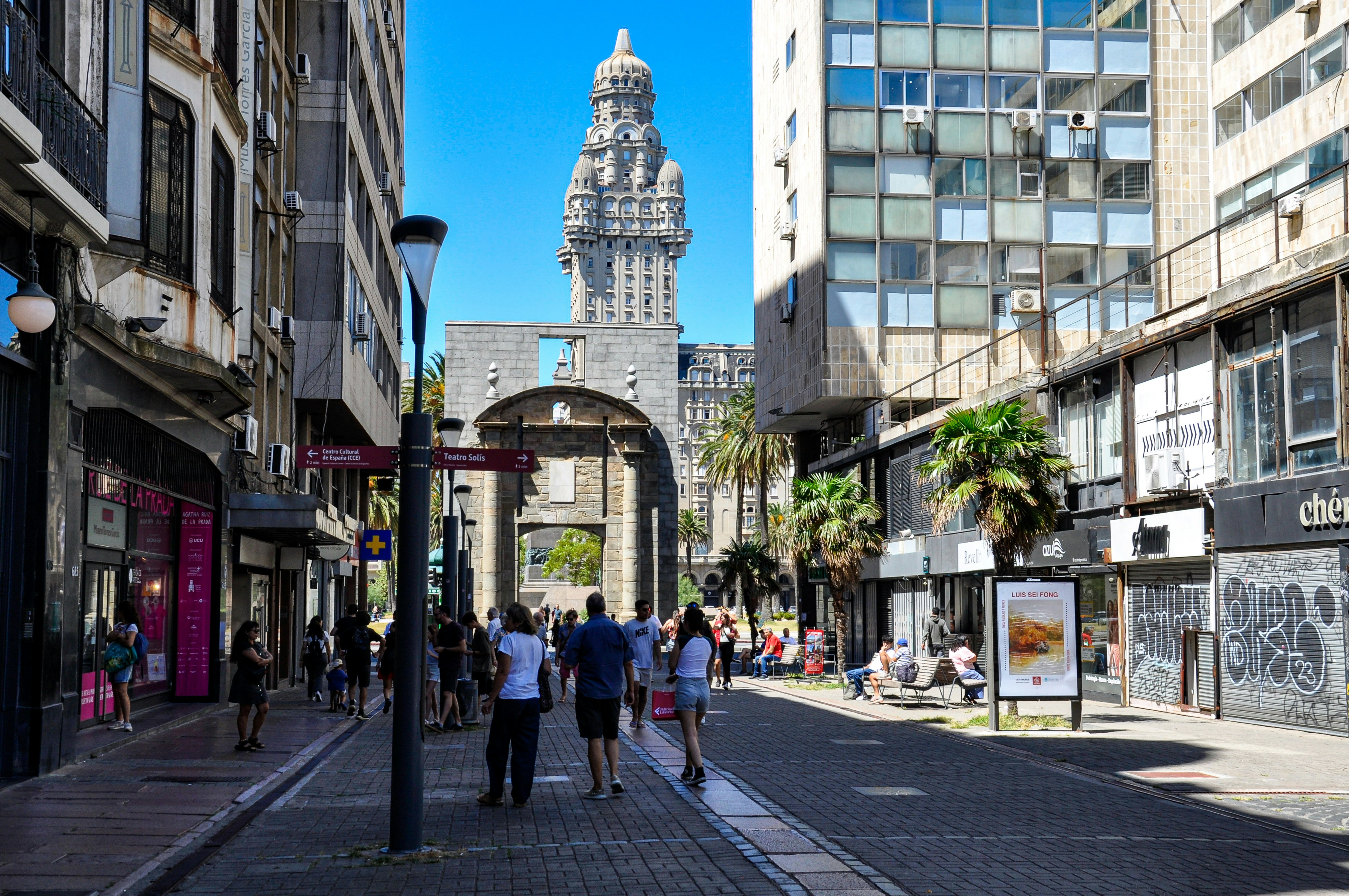 As pessoas caminham por uma rua em direção a um grande monumento.