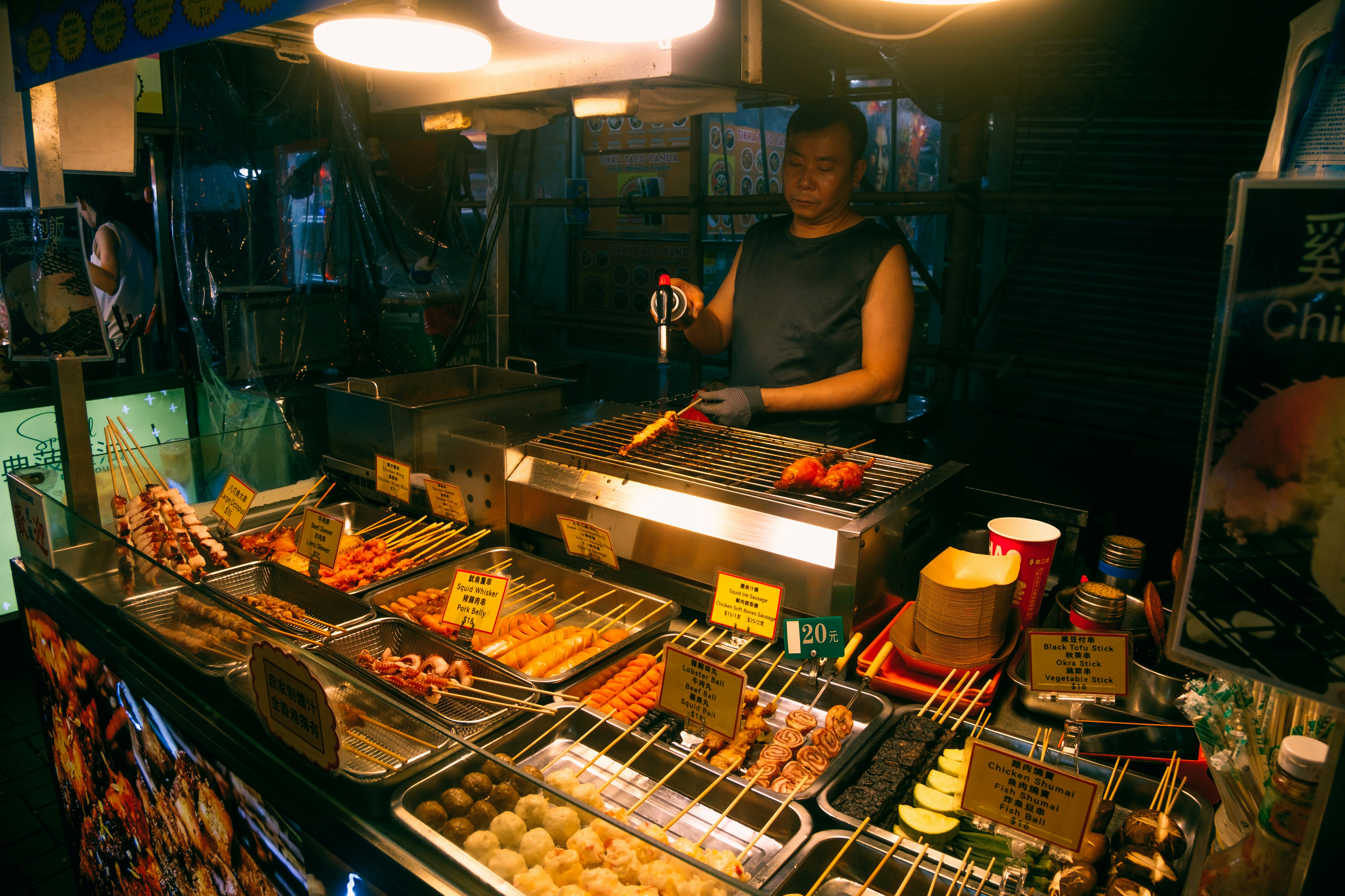 Un vendeur cuisine des brochettes à un stand de marché nocturne.