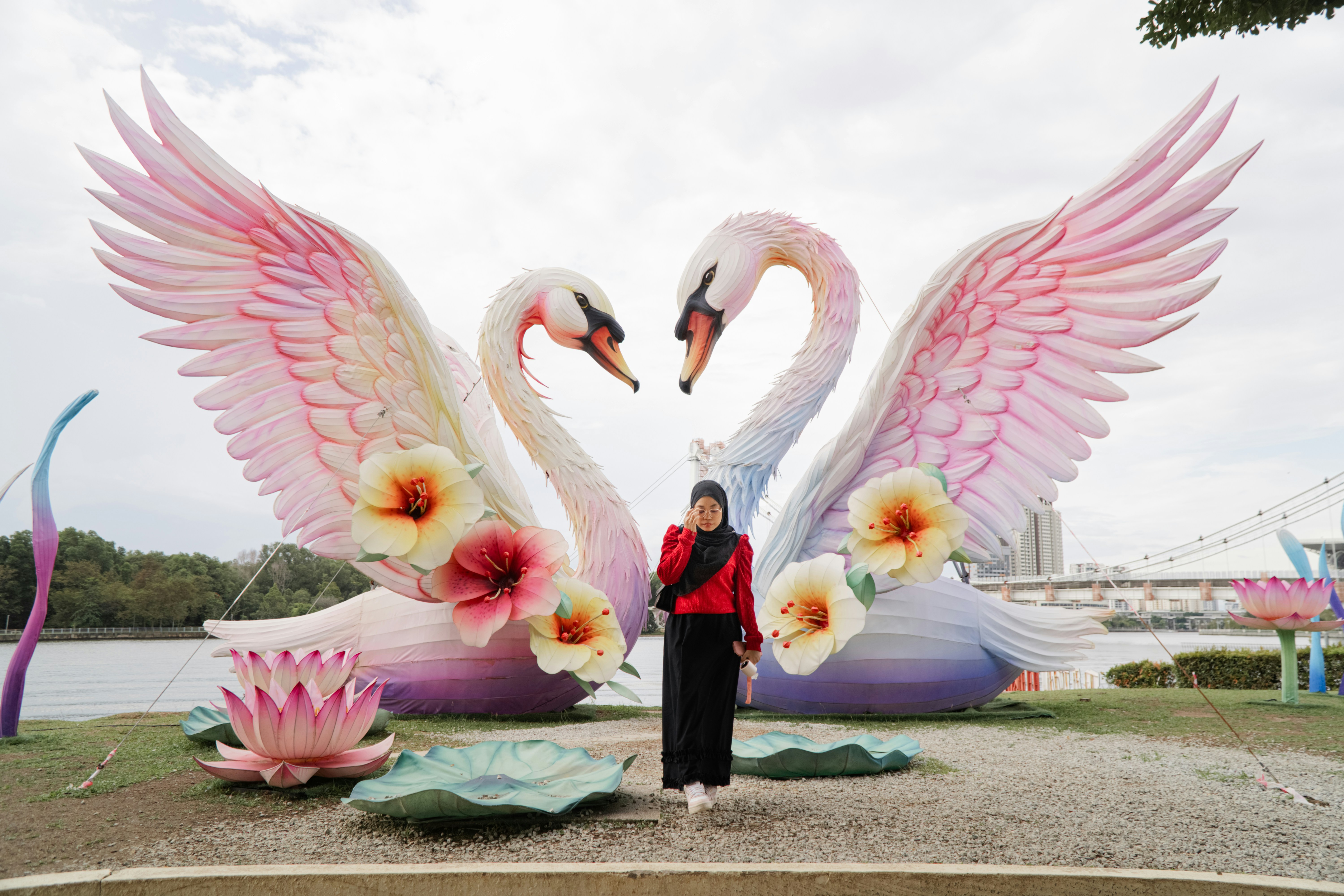 A person stands before a large swan sculpture with flowers.