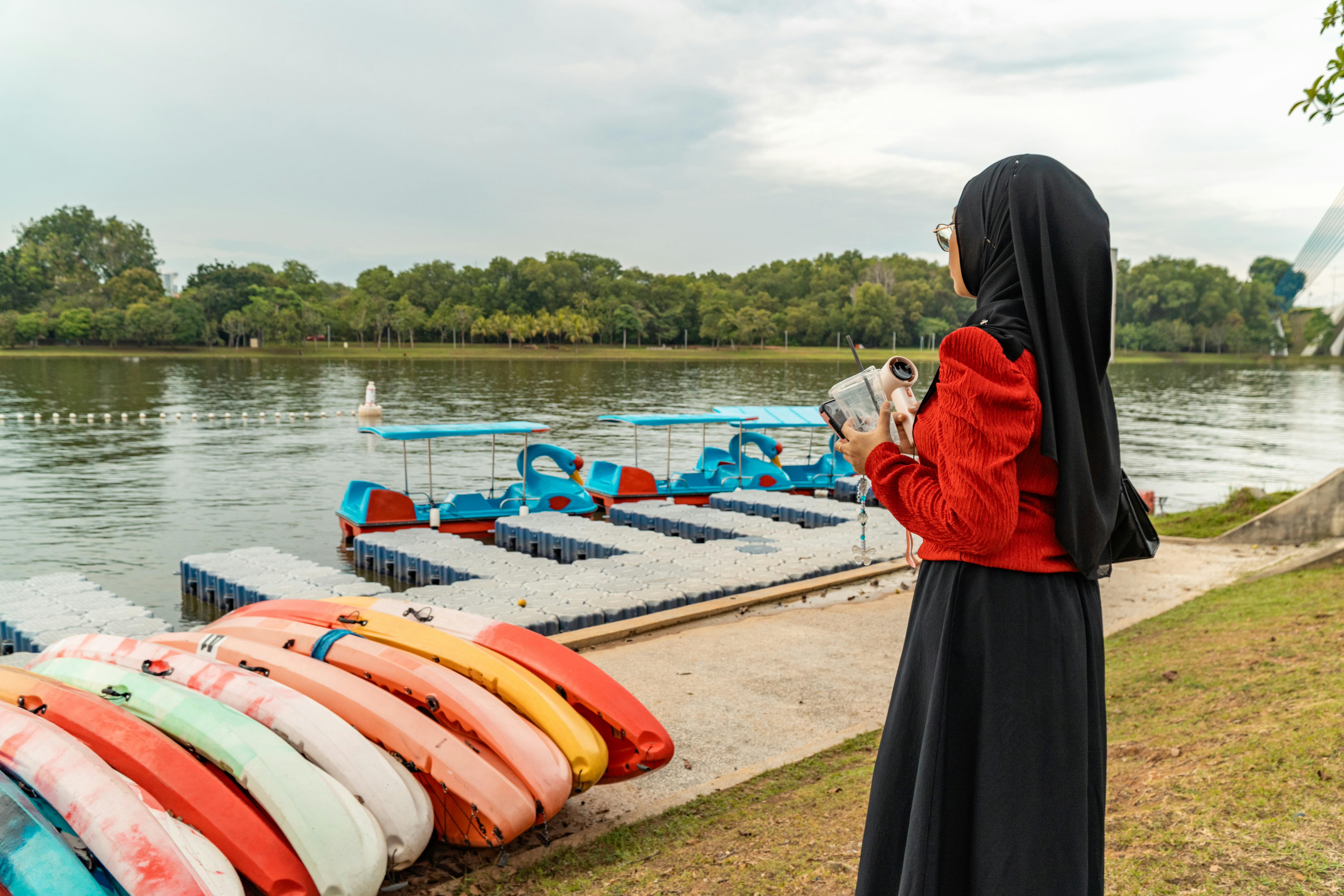 Woman in hijab by a lake with colorful kayaks