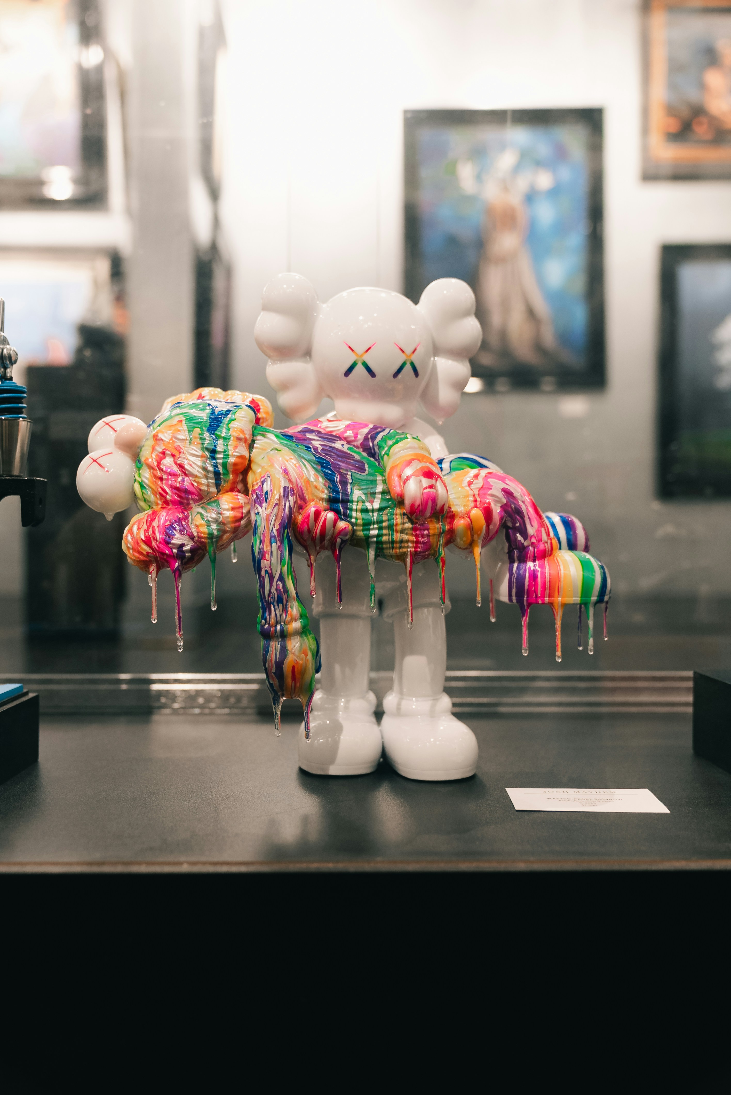 Figura blanca de kaws cubierta de pintura colorida y goteante.