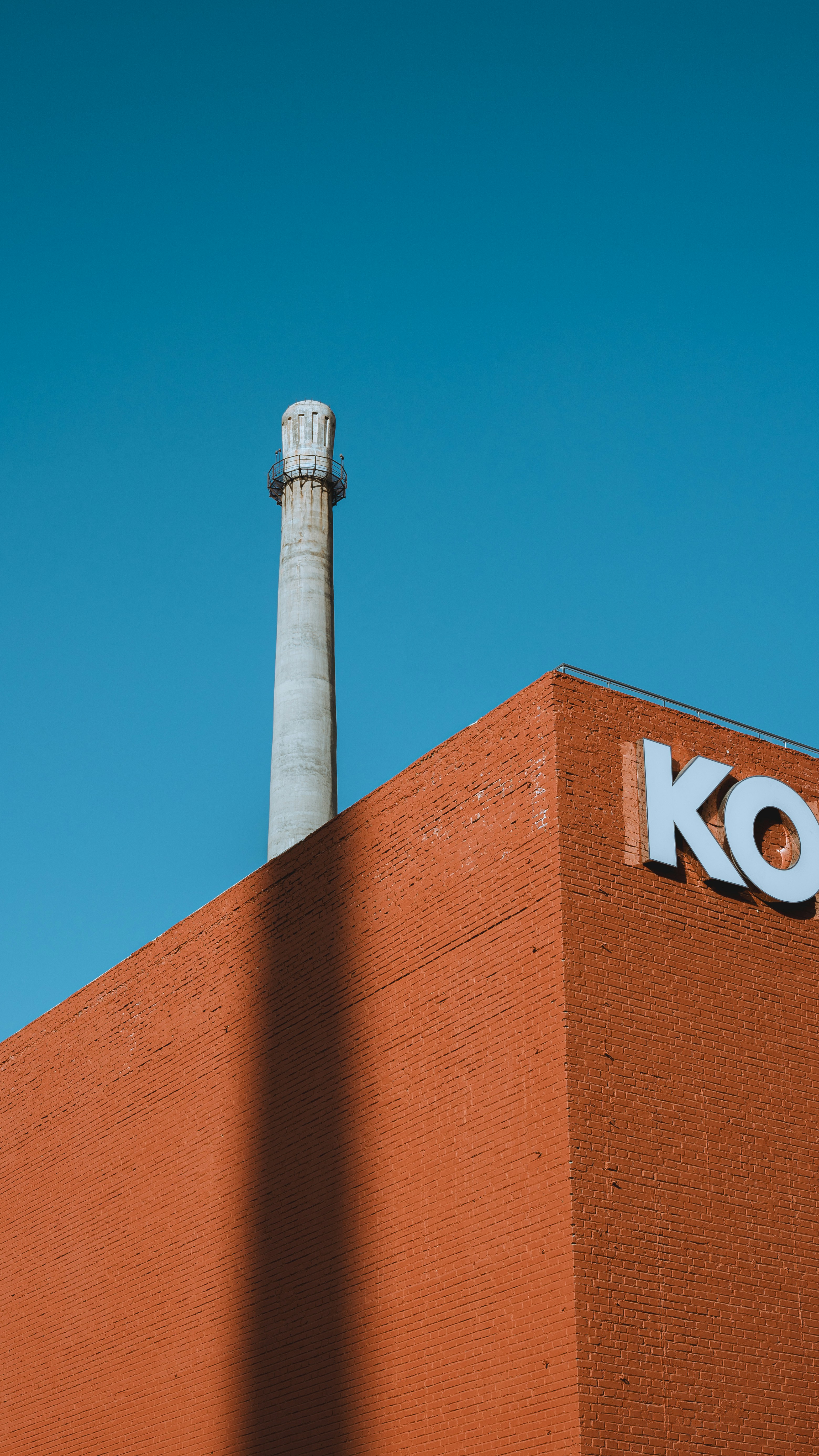 Orangefarbenes Backsteingebäude mit einem hohen Schornstein gegen den blauen Himmel