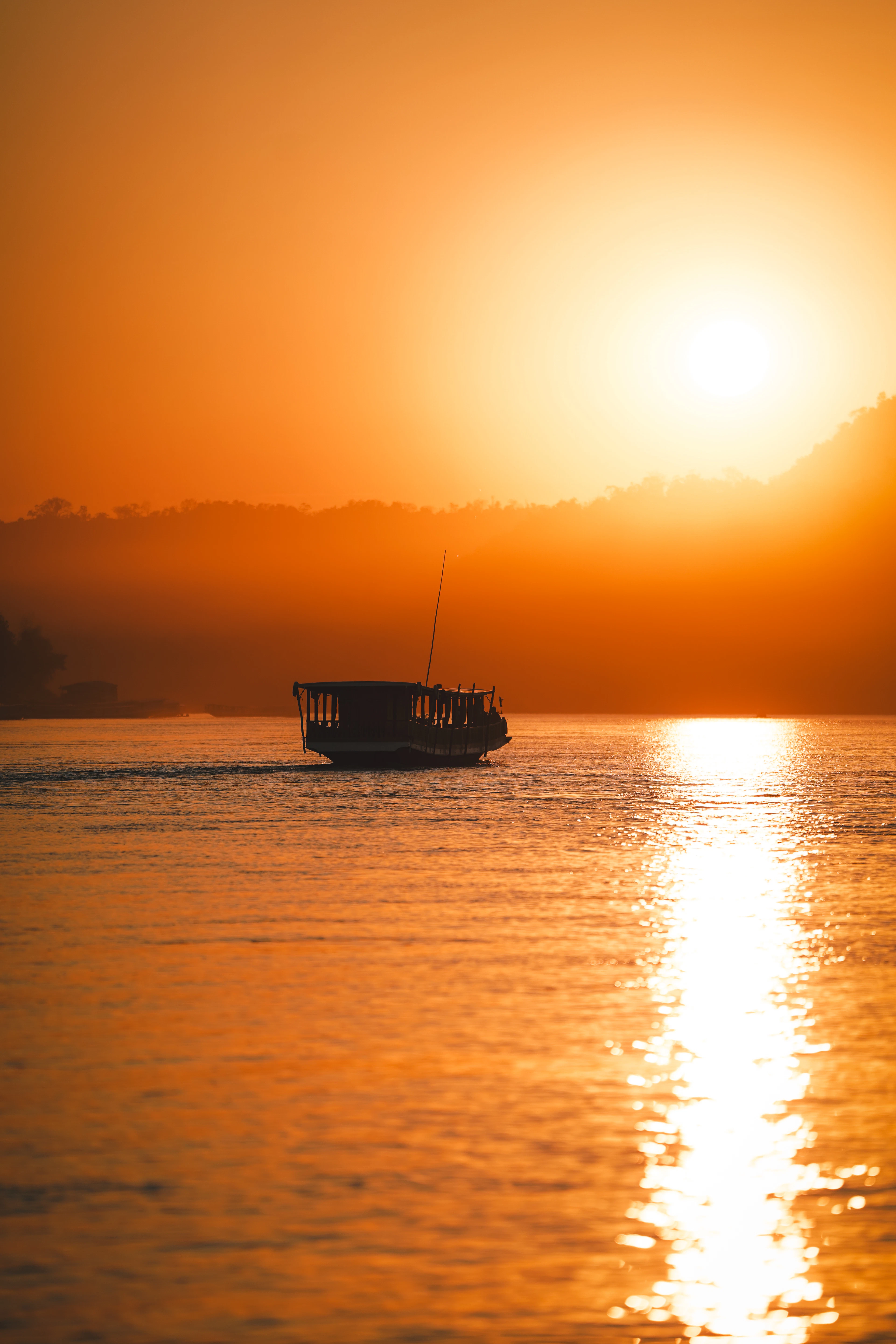 A silhouetted boat glides across the Mekong River under a glowing orange sunset.