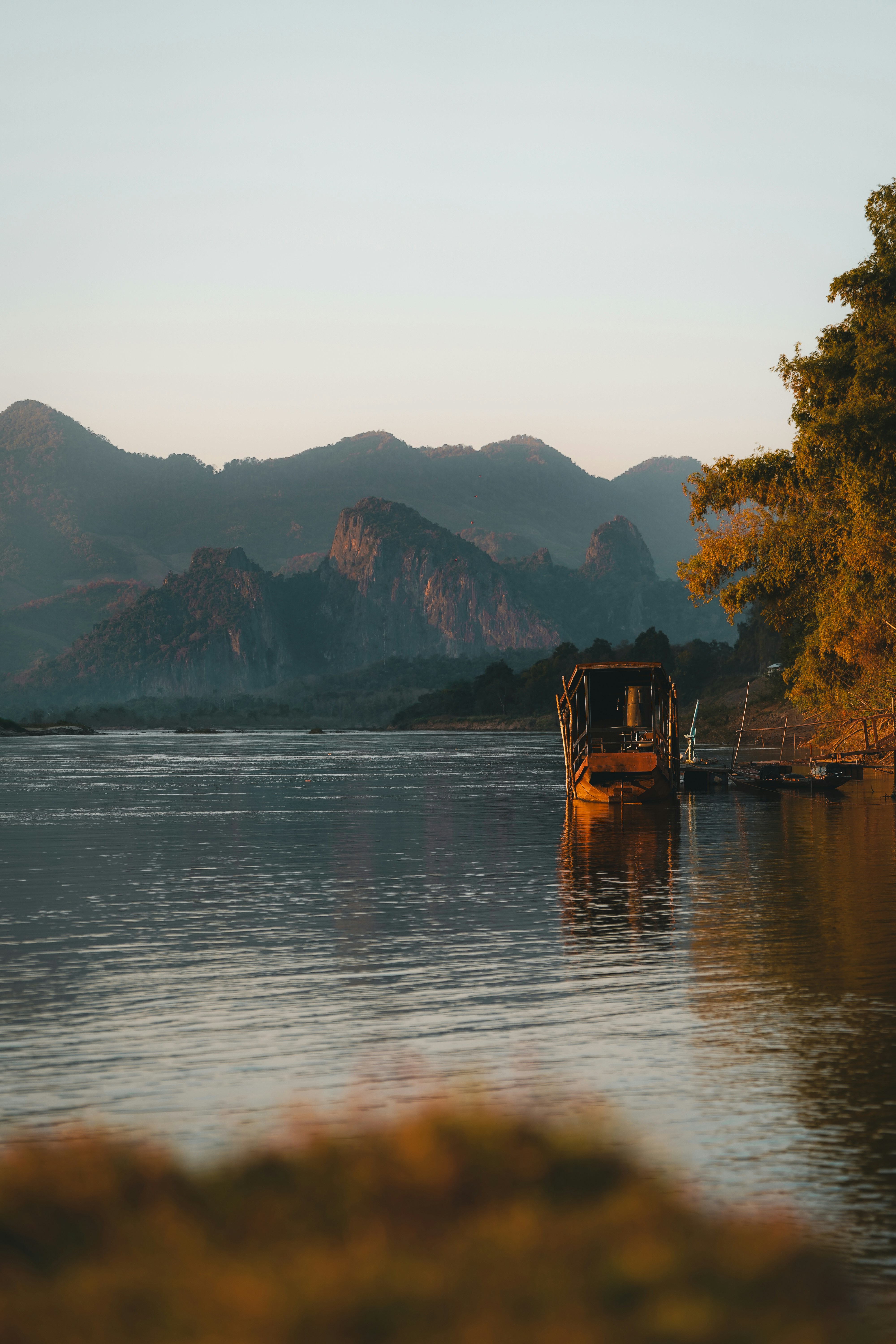 Rusty boat docked on a calm lake with mountains.