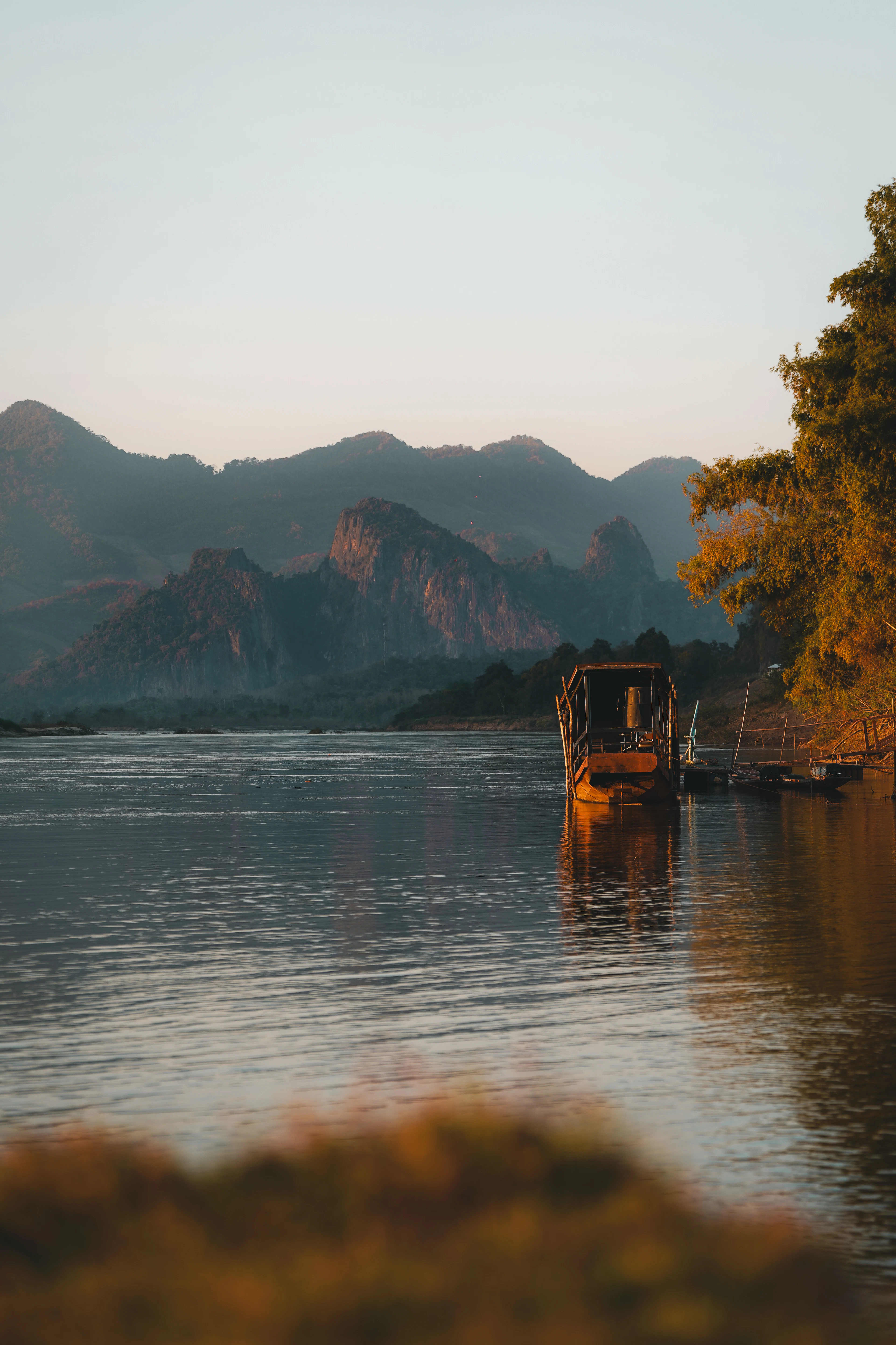 Dusk over the Mekong River with a jagged mountain silhouette and a moored boat dock.